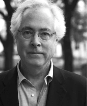 Black and white photo of a man with glasses, light-colored hair, wearing a suit jacket and collared shirt, outdoors