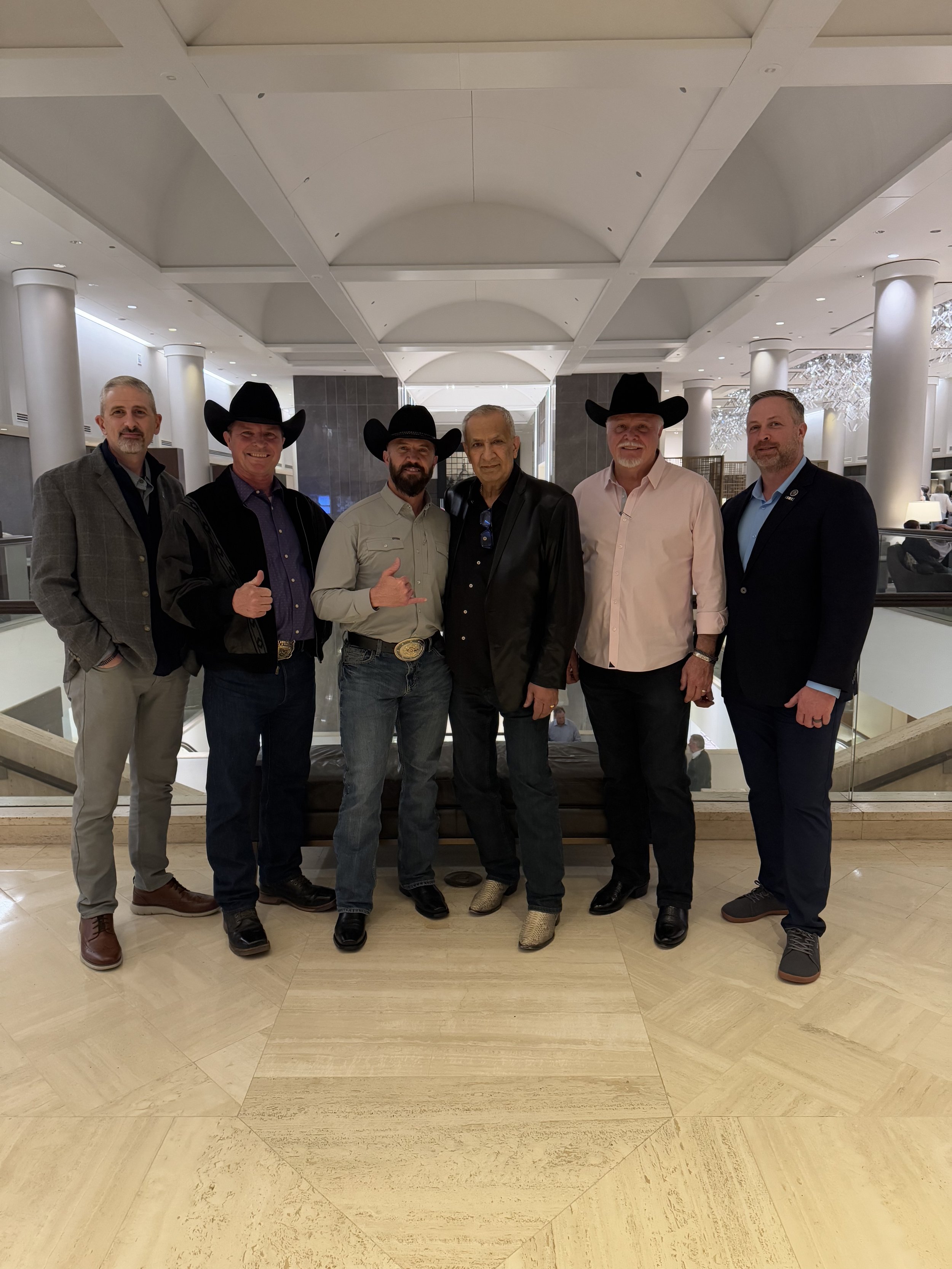Group of six men dressed in formal and cowboy attire standing in a hotel lobby.