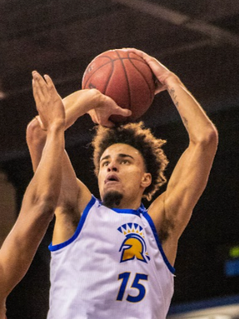 A basketball player in a white and blue jersey with the number 15, preparing to shoot or pass during a game.