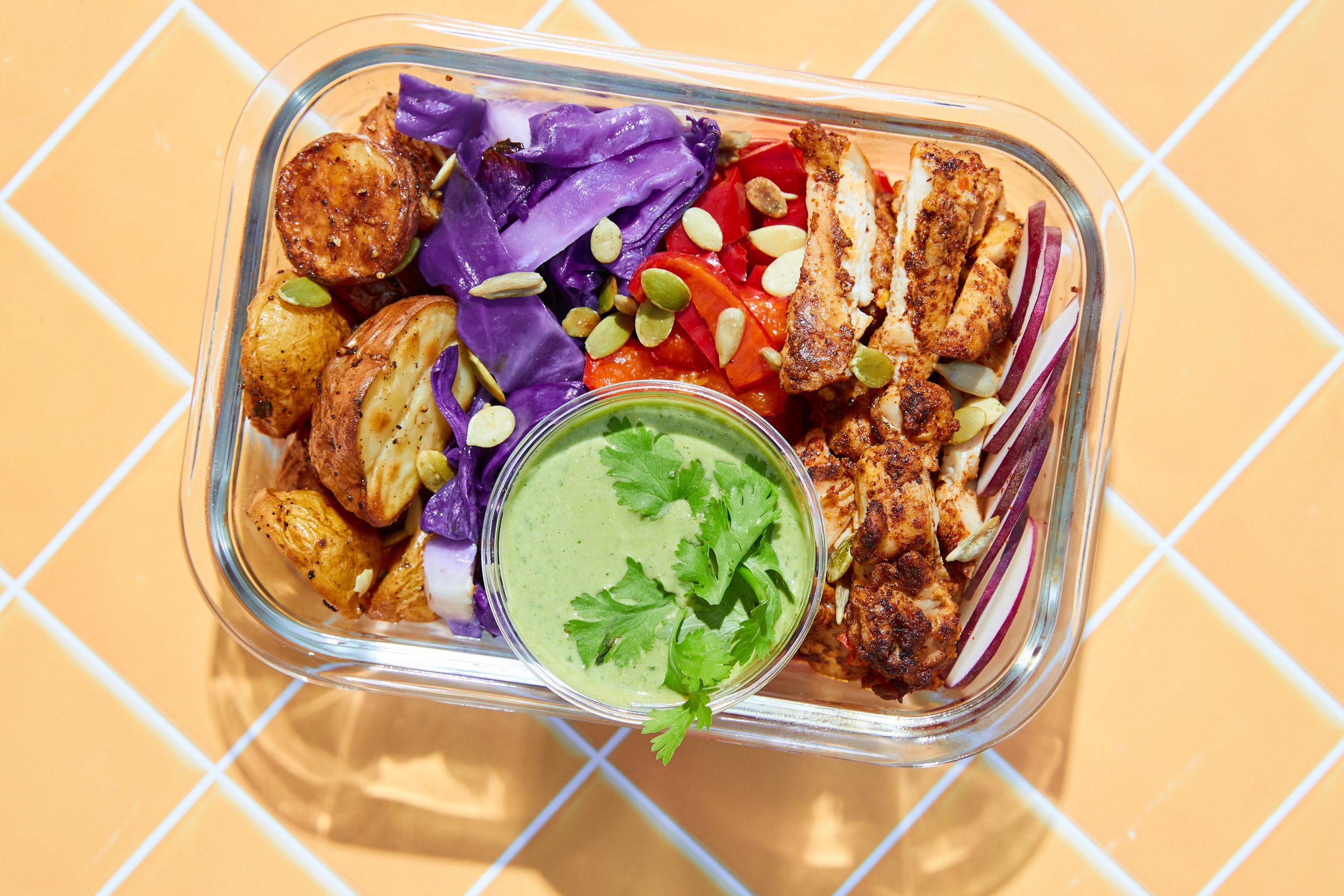 Gather Around Nutrition meal prep container with perfectly portioned chicken, golden potatoes, vibrant vegetables, and signature sauce, demonstrating how our chef-crafted meals deliver complete nutrition with gourmet flavor in a convenient ready-to-e