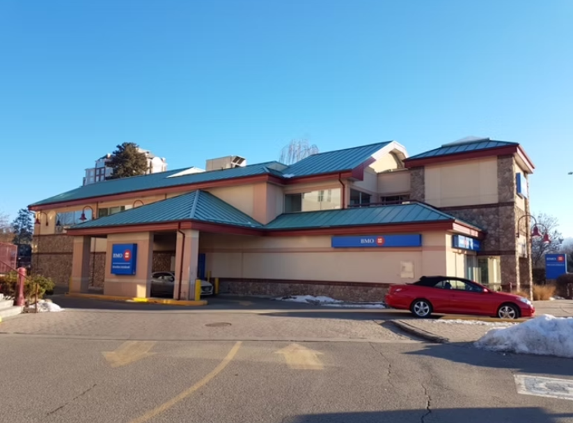 BMO bank branch building with a red car parked in front, on a clear day with patches of snow on the ground.