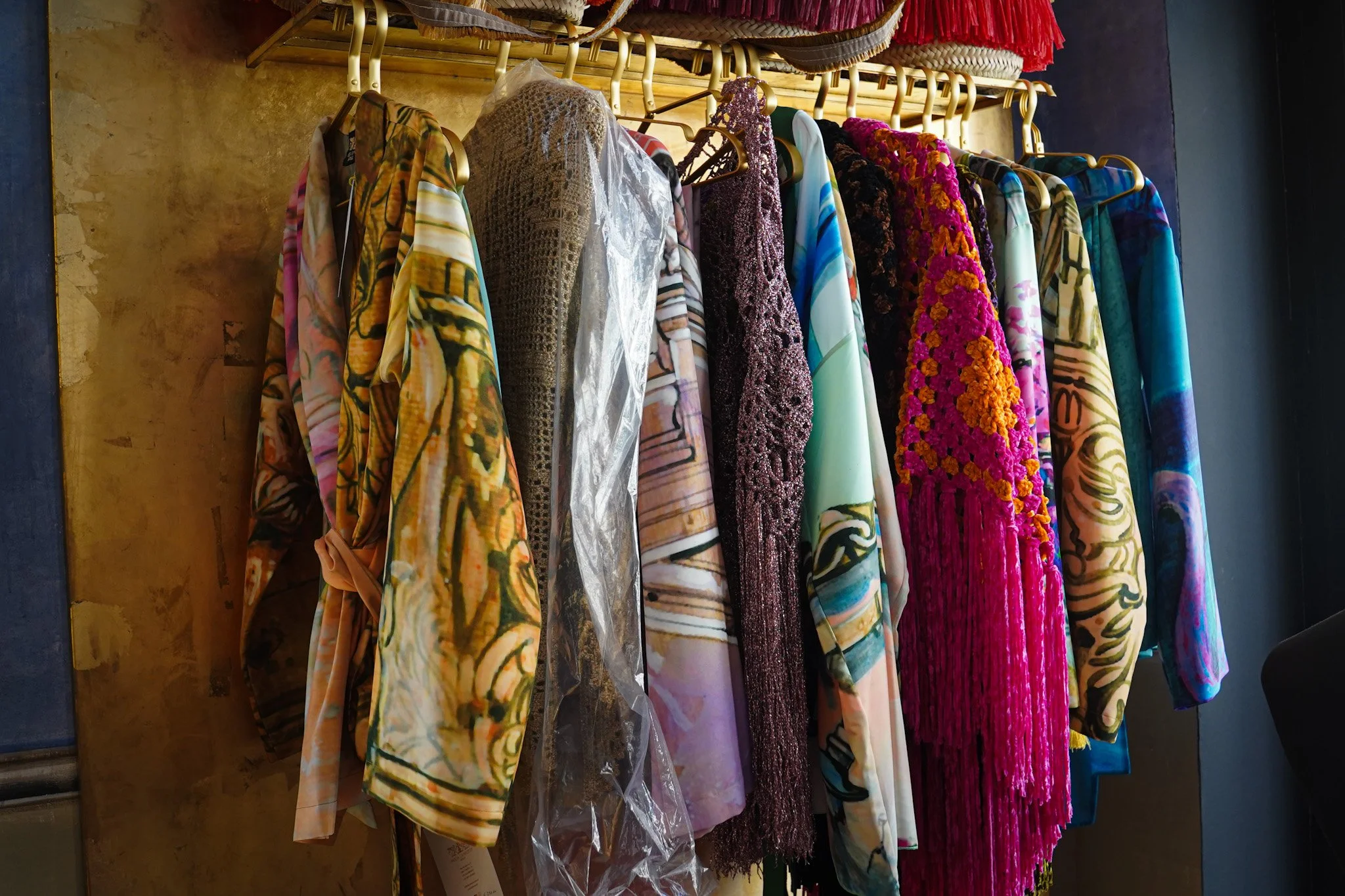 Colorful clothing rack with various fabrics including crocheted, fringed, and printed materials.