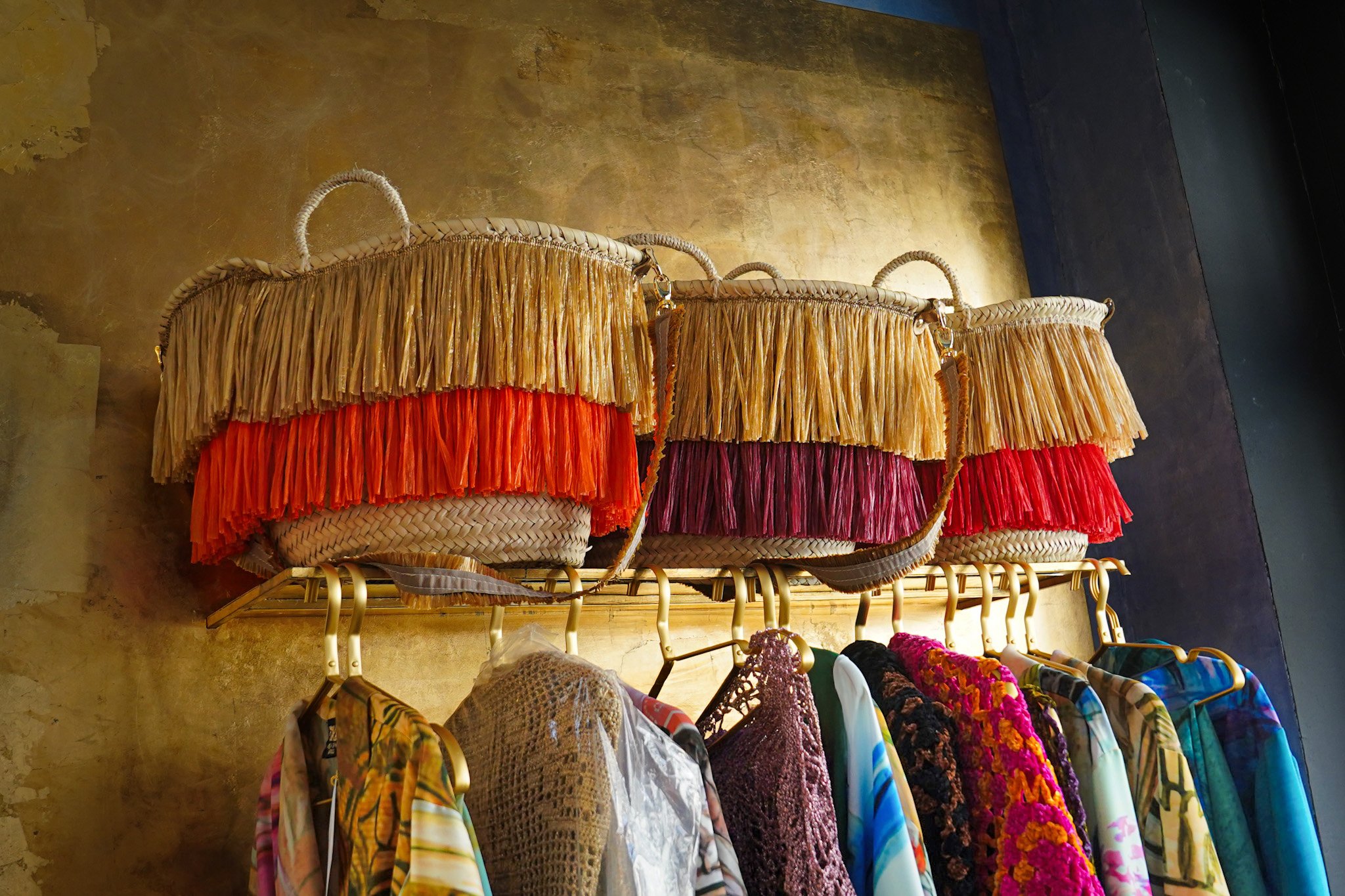 Colorful fringed handbags and assorted clothing hanging on a rack.