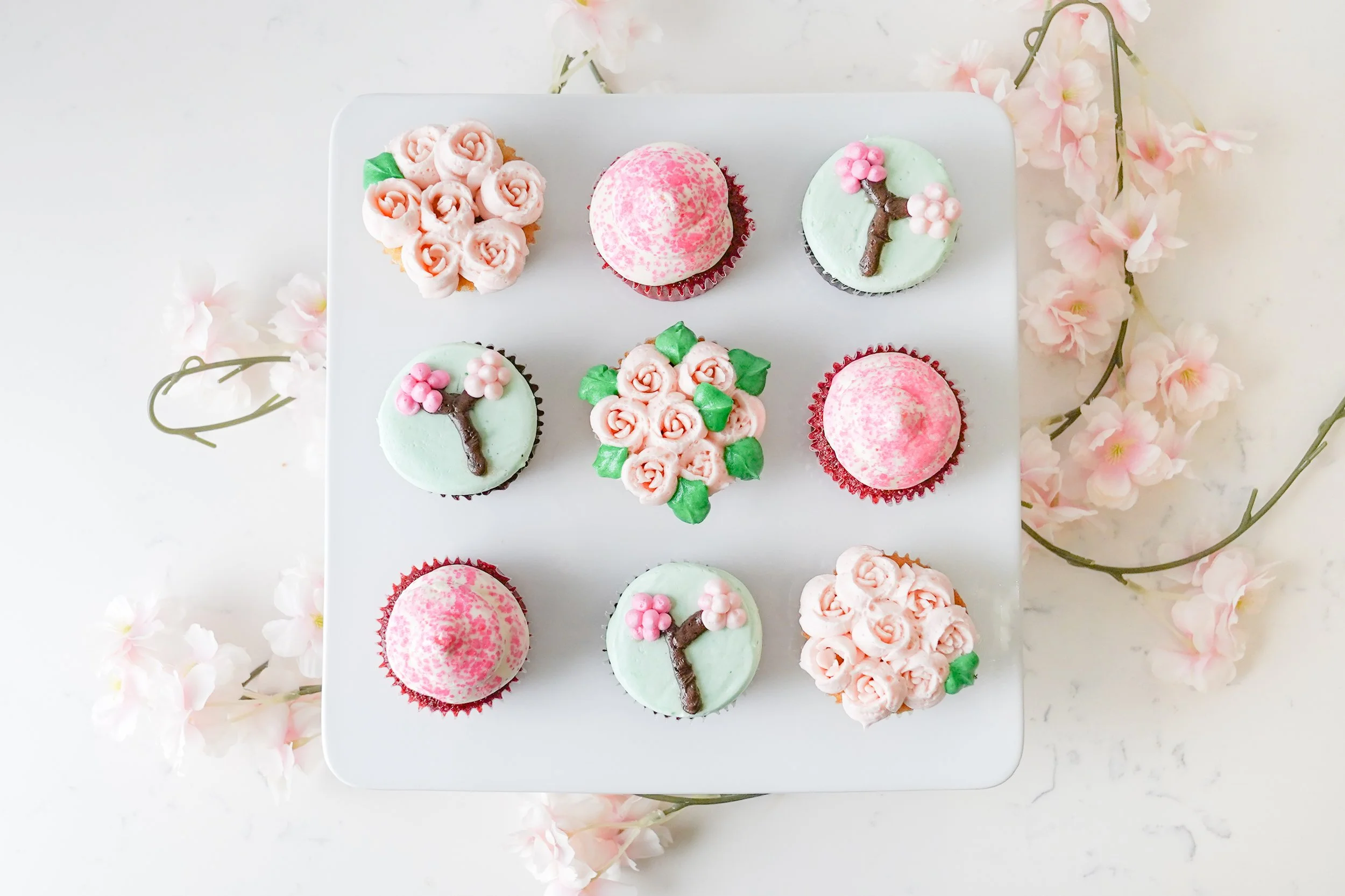 Cupcakes decorated with pink cherry blossom designs and flowers on a white background.