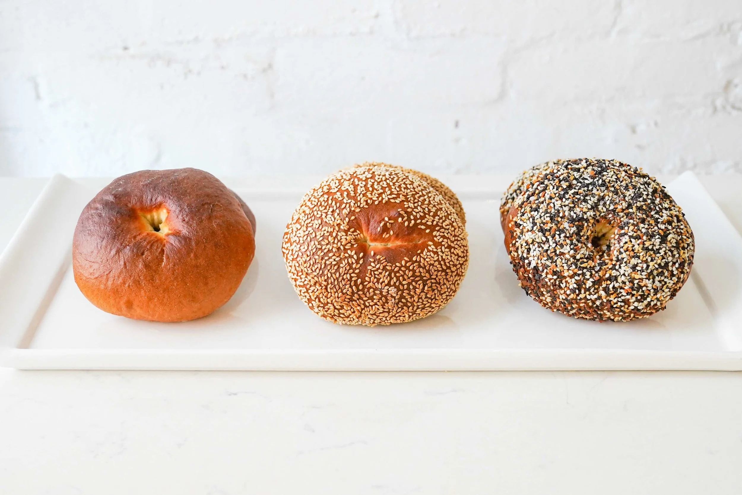 Three bagels on a white tray: plain, sesame seed, and everything bagel.