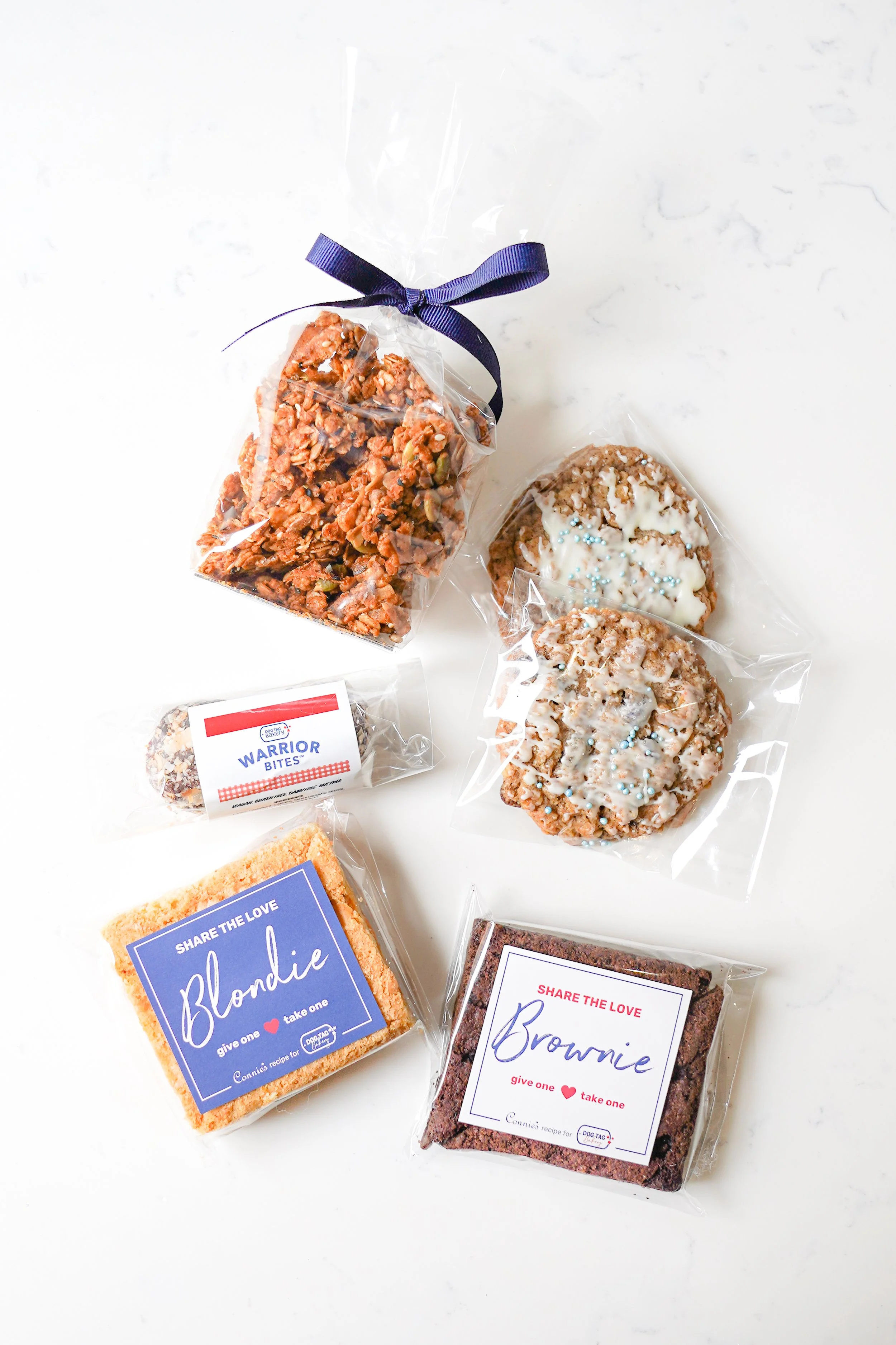 Various packaged snacks including cookies, brownie, blondie, and granola mix on a white surface.