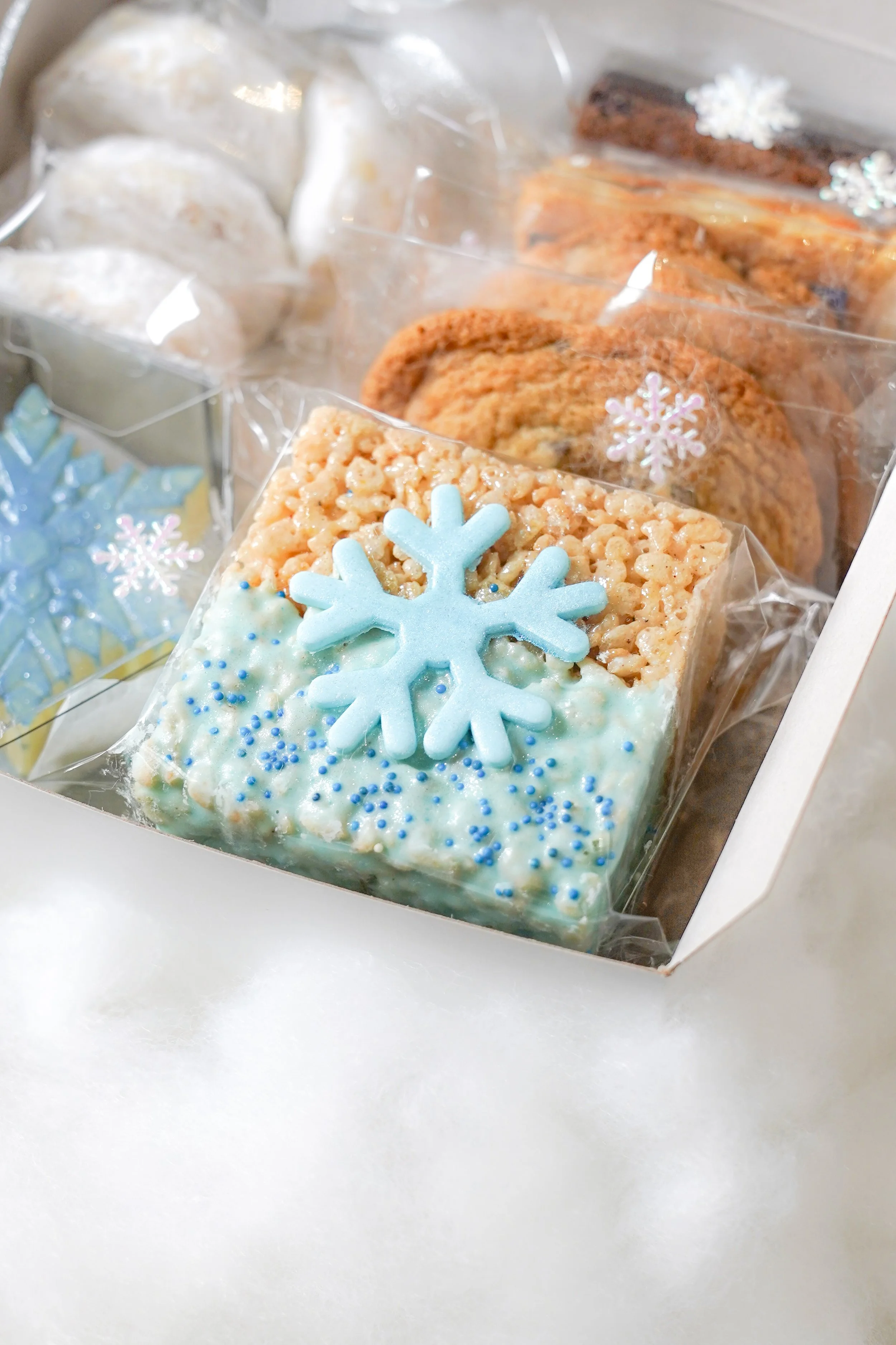Assorted cookies and rice krispie treats with snowflake decorations in a box.