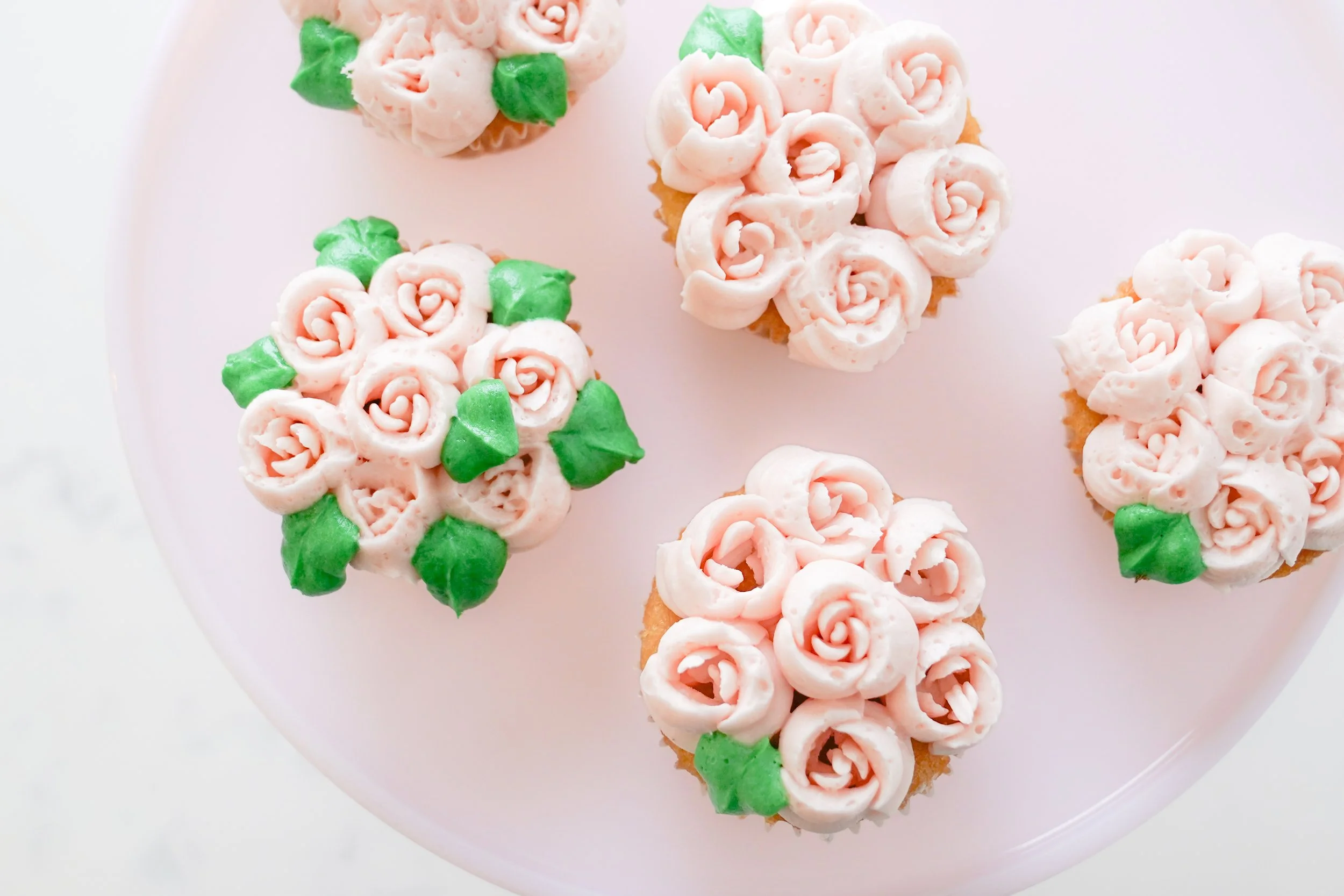 Cupcakes with pink rose-shaped frosting and green leaves on a white background.