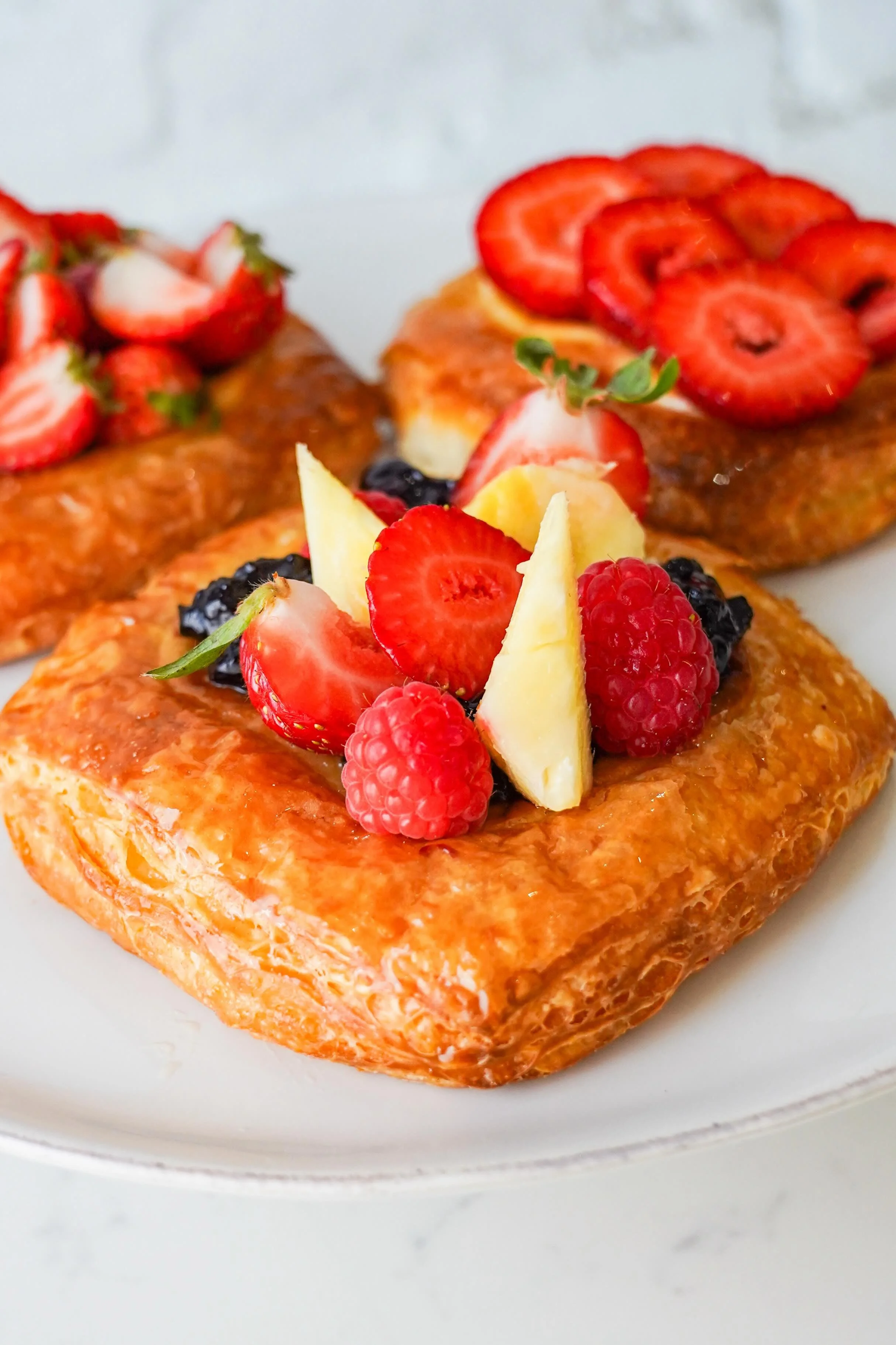 Assorted fruit pastries topped with strawberries, raspberries, and other berries on a plate.