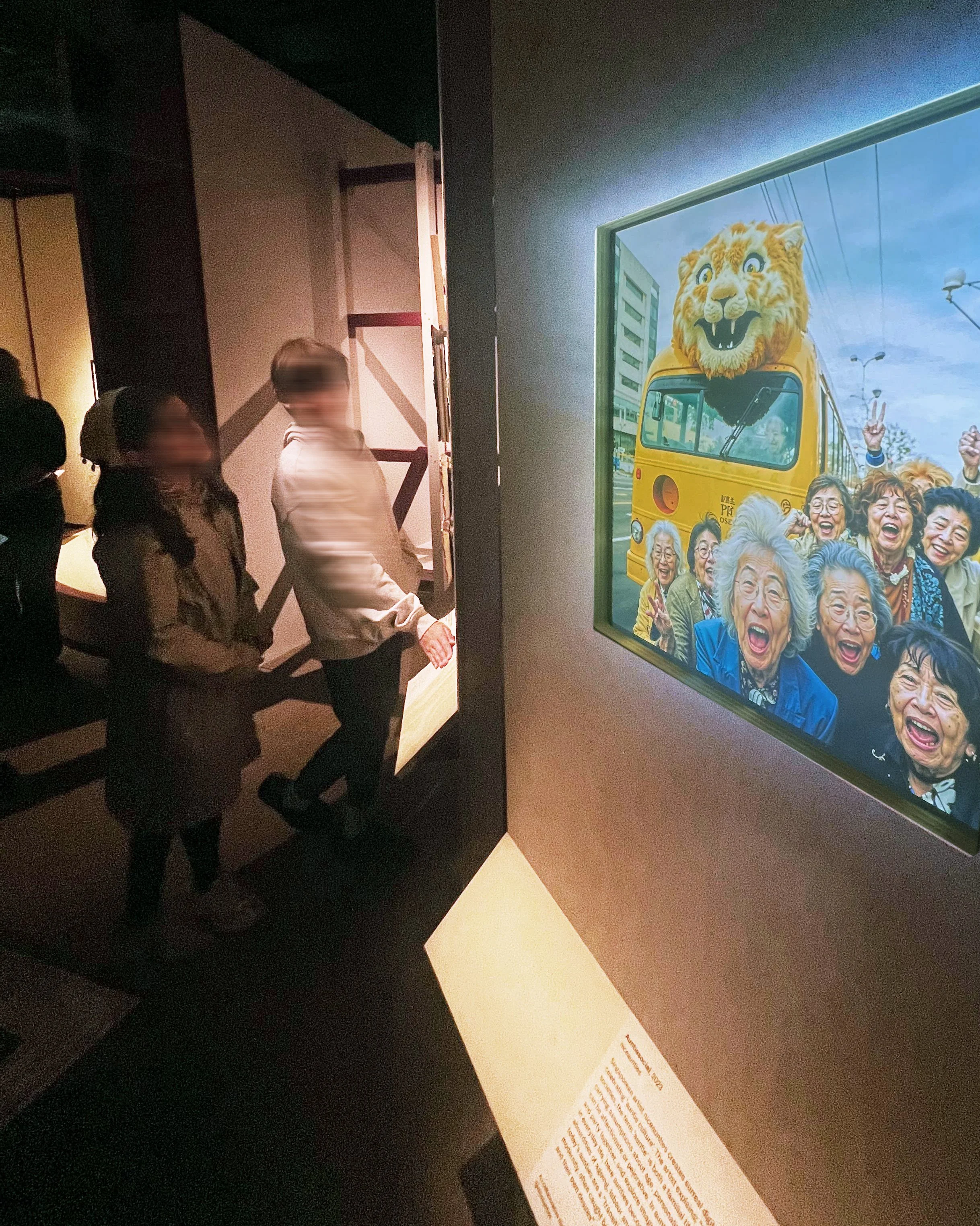 People viewing an art display at a museum, with a vivid illustration of a smiling lion-headed subway train and a group of laughing elderly women on a blue sky background.