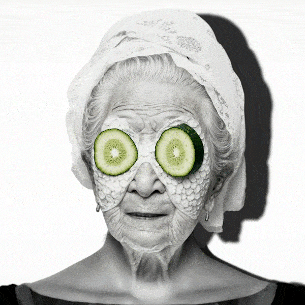An elderly woman's face with cucumber slices over her eyes, digital effects resembling ice cream and lettuce on her cheeks, black and white filter, head wrapped in a towel, with a shadow cast on the right side.