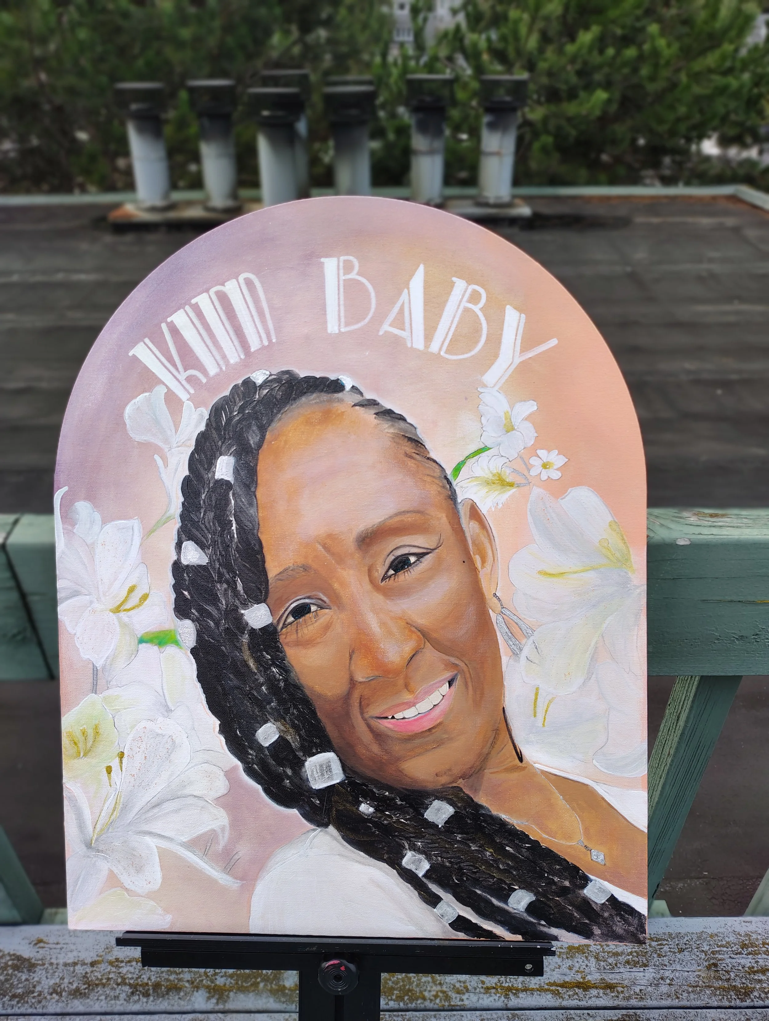 Portrait painting of a woman with braided hair, surrounded by white flowers, displayed outdoors on a rooftop with trees in the background.