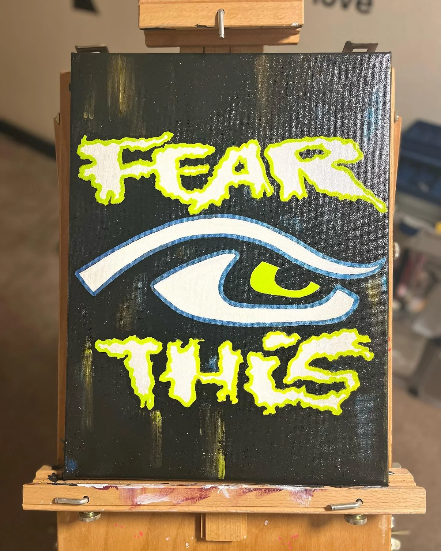 Canvas with "FEAR THIS" in neon lettering and an eye design on an easel, hand painted by PleasantArt