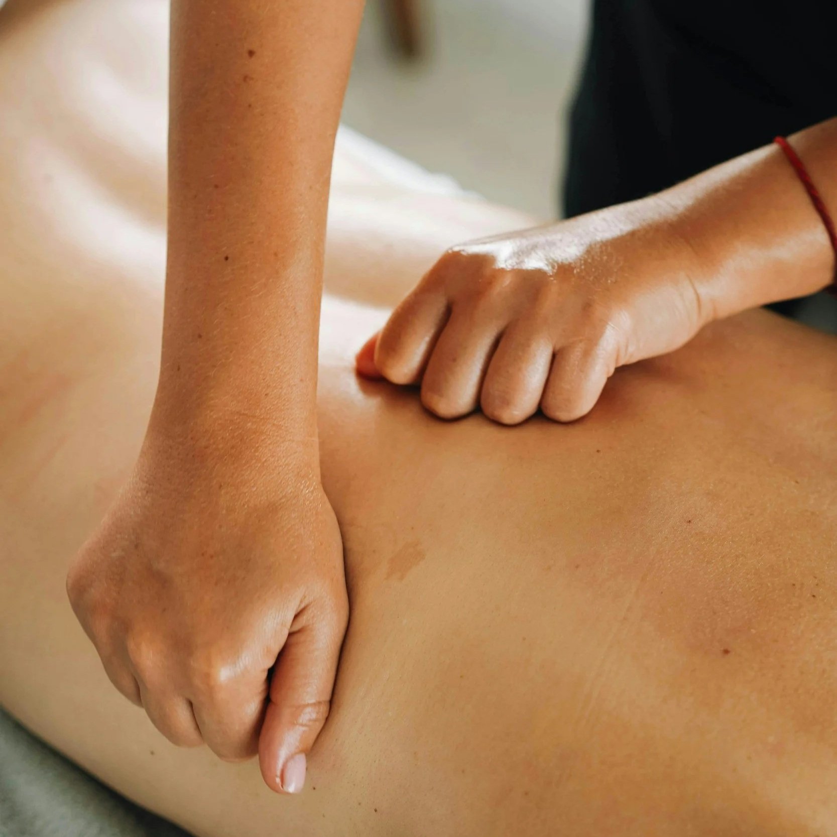 Close-up of a person's hand massaging or pressing on another person's back, with focus on the hand and skin. The scene appears to be a massage or skin therapy session.