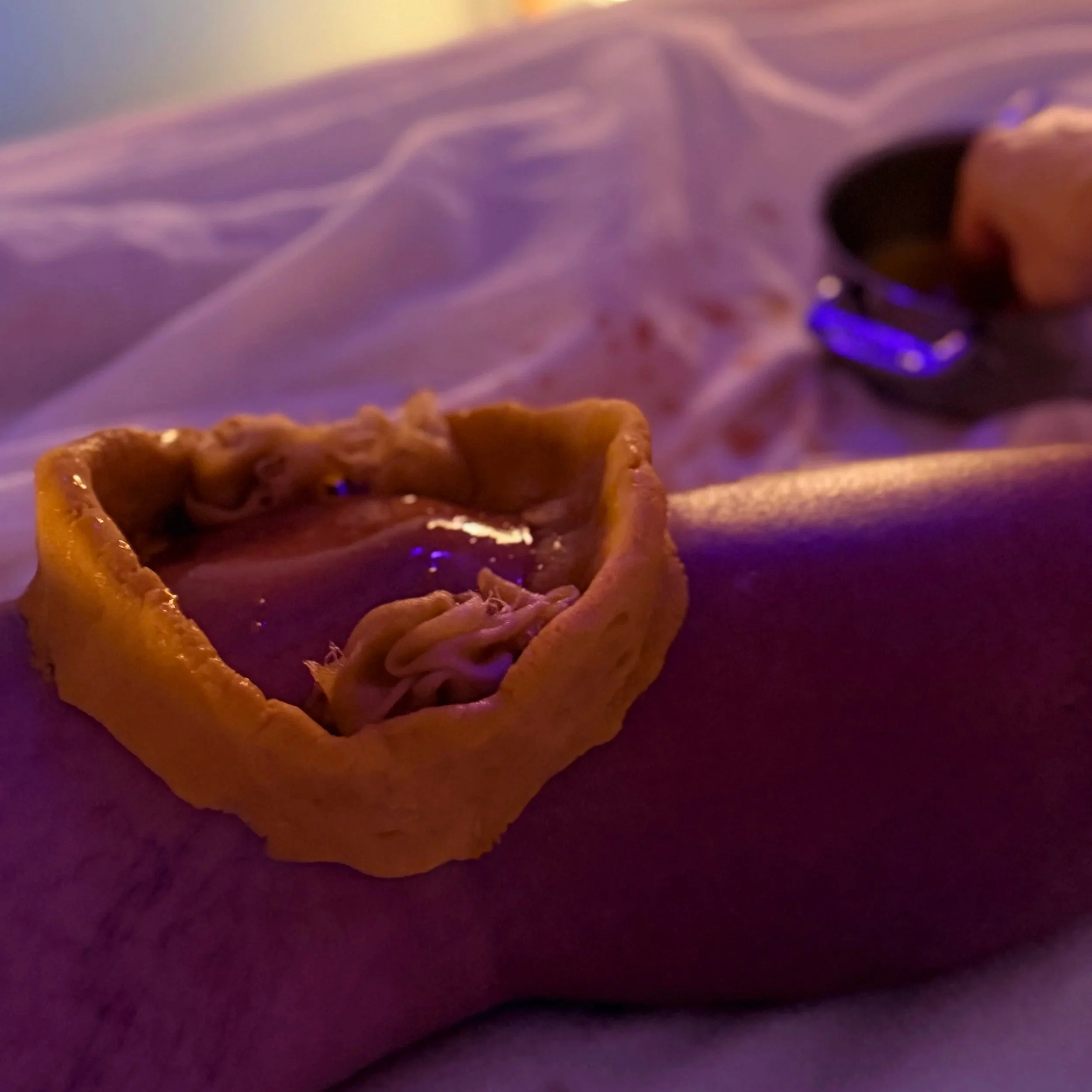 A close-up of a person wearing a black smartwatch bending over a purple surface with a small square-shaped object in front of them under purple and yellow lighting.