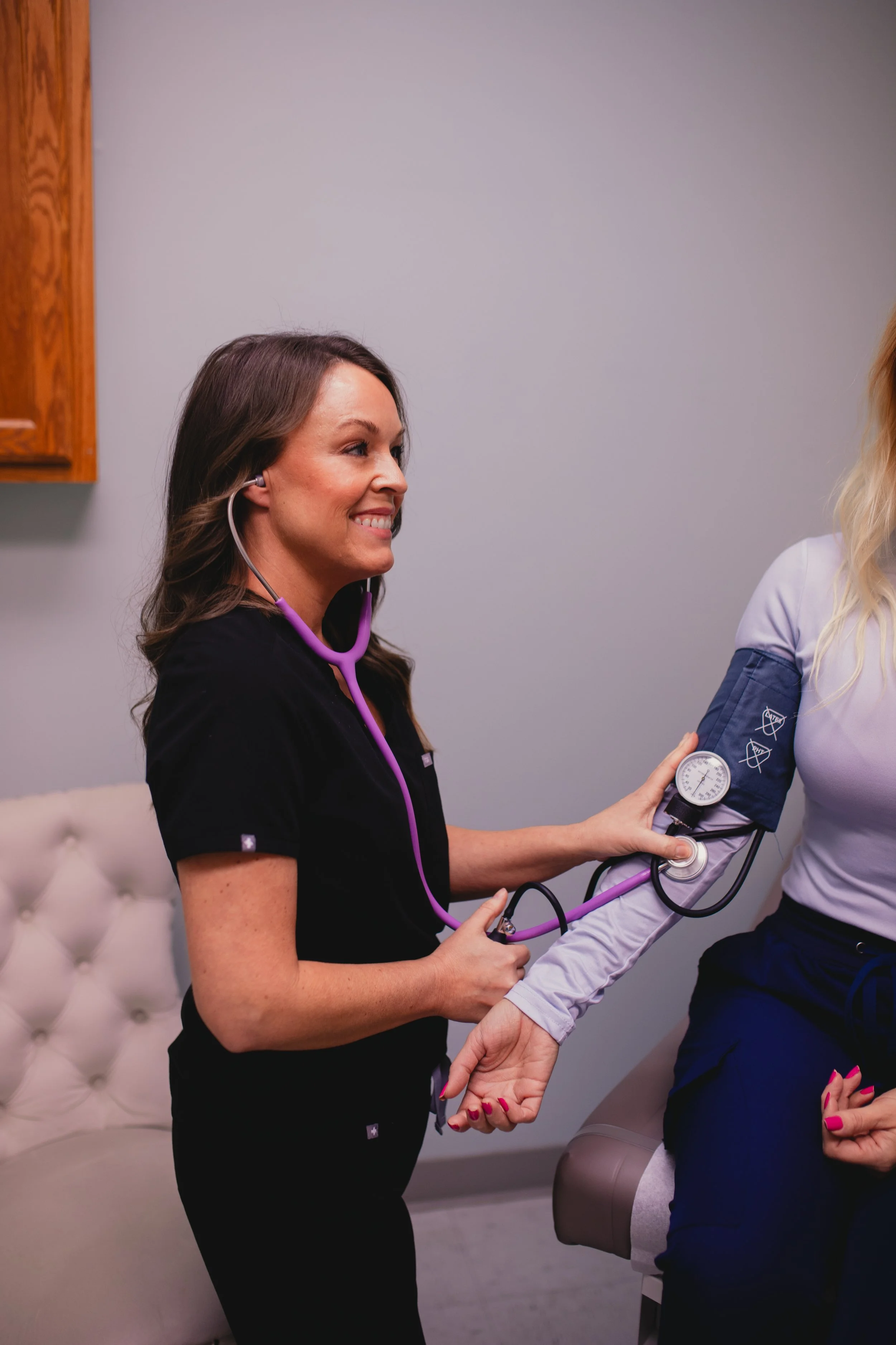 A healthcare professional in black scrubs using a stethoscope to check a patient's blood pressure in a clinic.