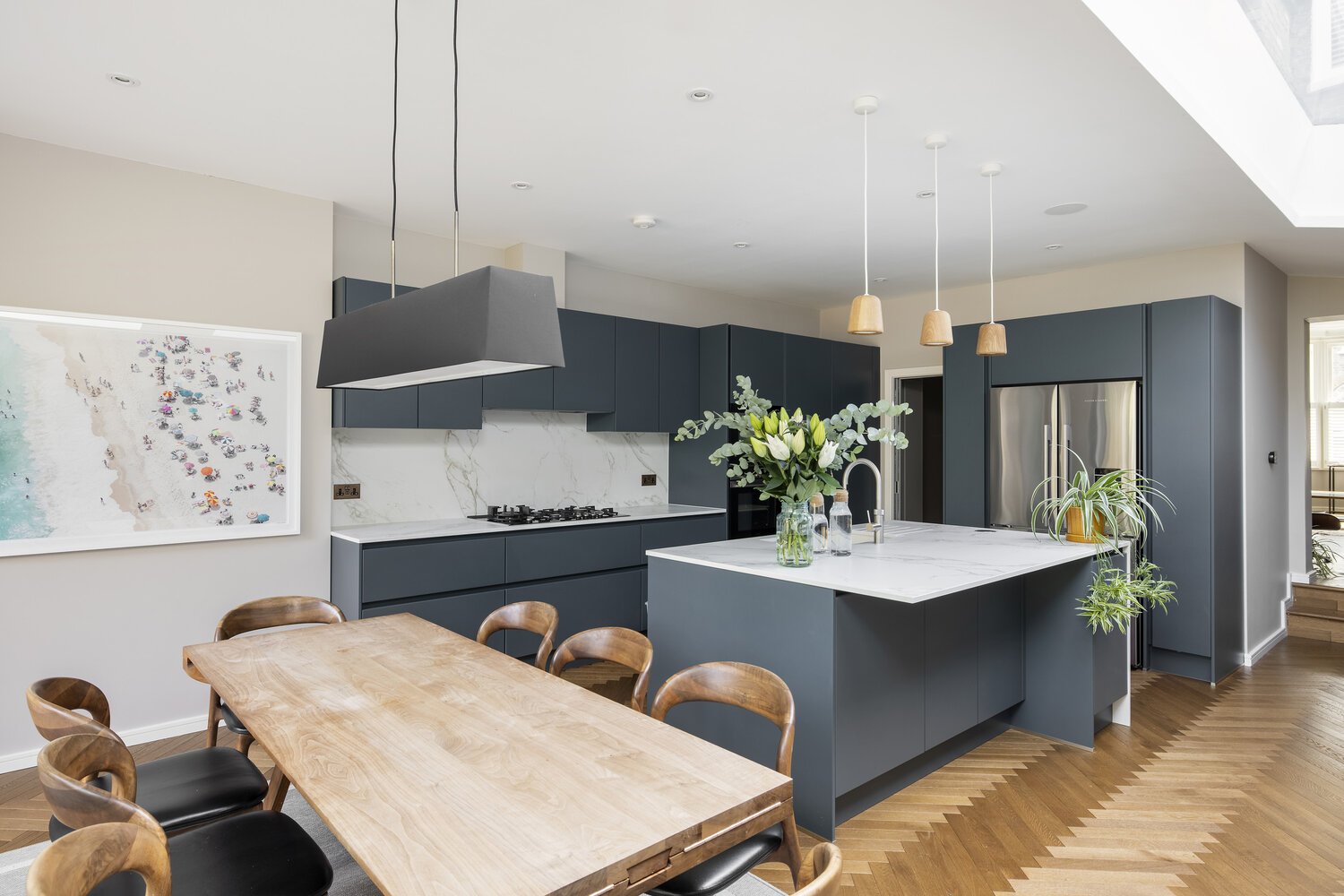  Kitchen Modern kitchen with dark blue cabinets, white marble countertops, a kitchen island with flowers, and wooden dining table with chairs.