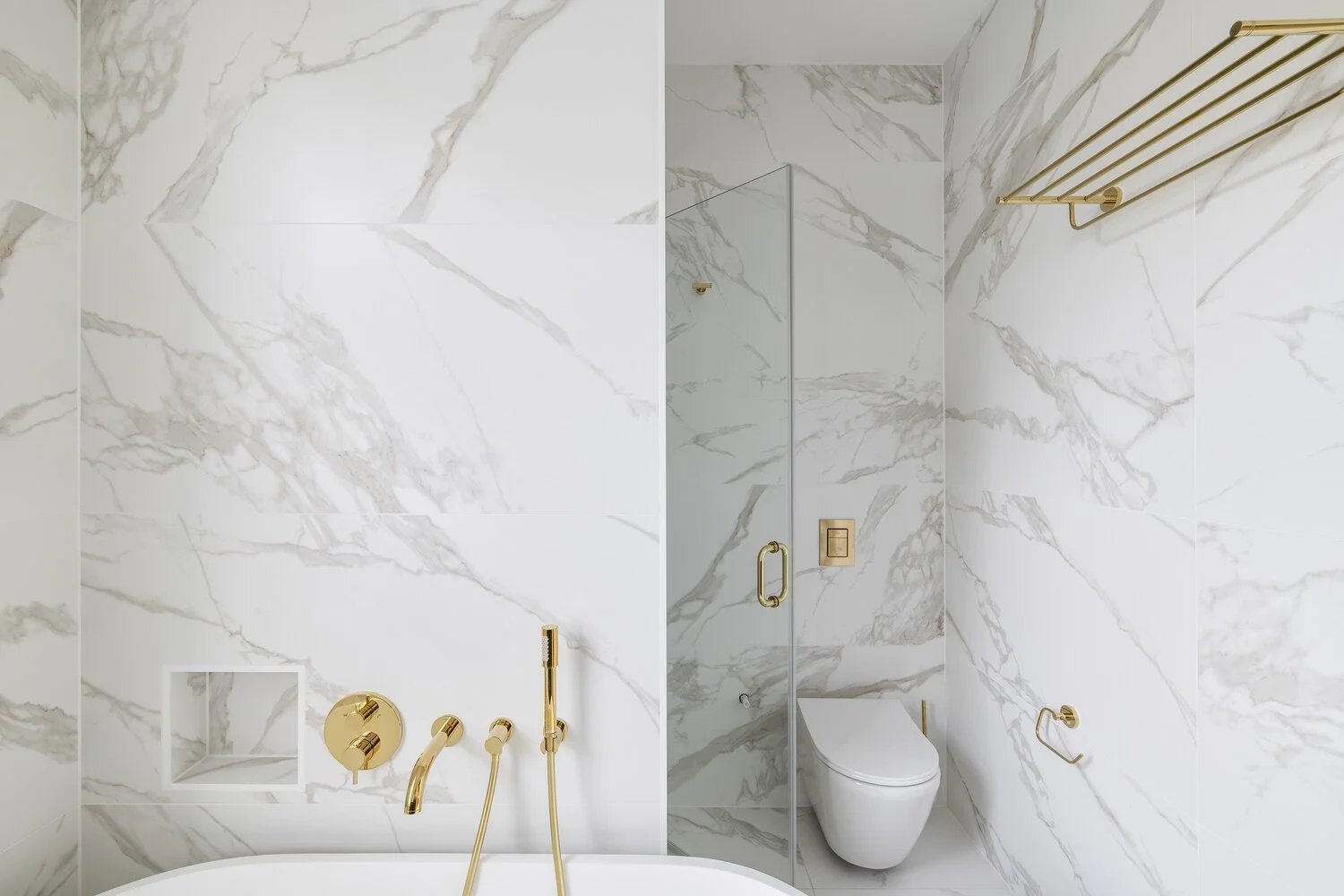  Bathroom Luxury bathroom with white marble walls, gold fixtures, and a modern toilet.