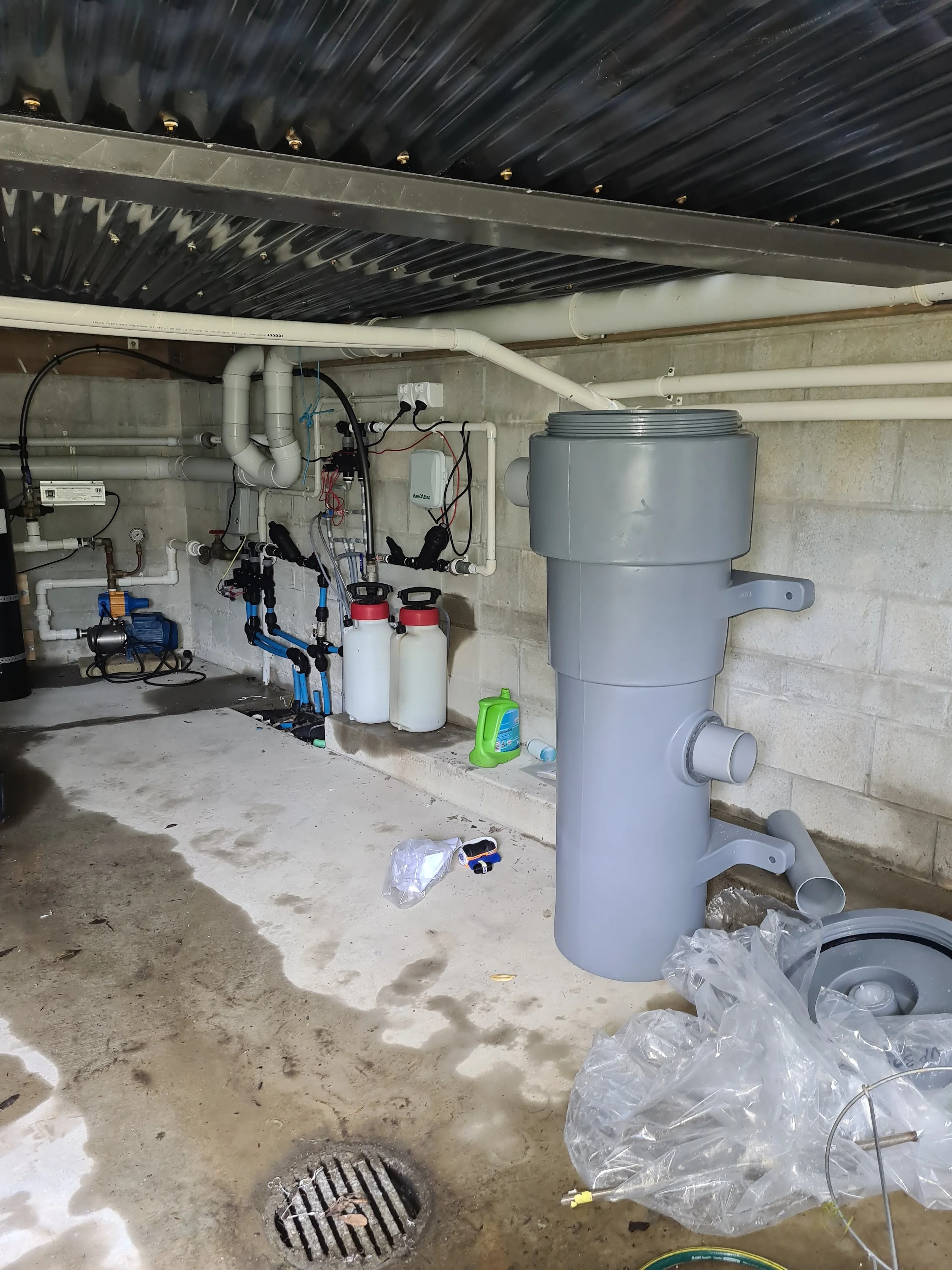 View of a basement with plumbing and equipment for a pool or spa system, including pipes, filters, and a large gray anti-vortex drain.