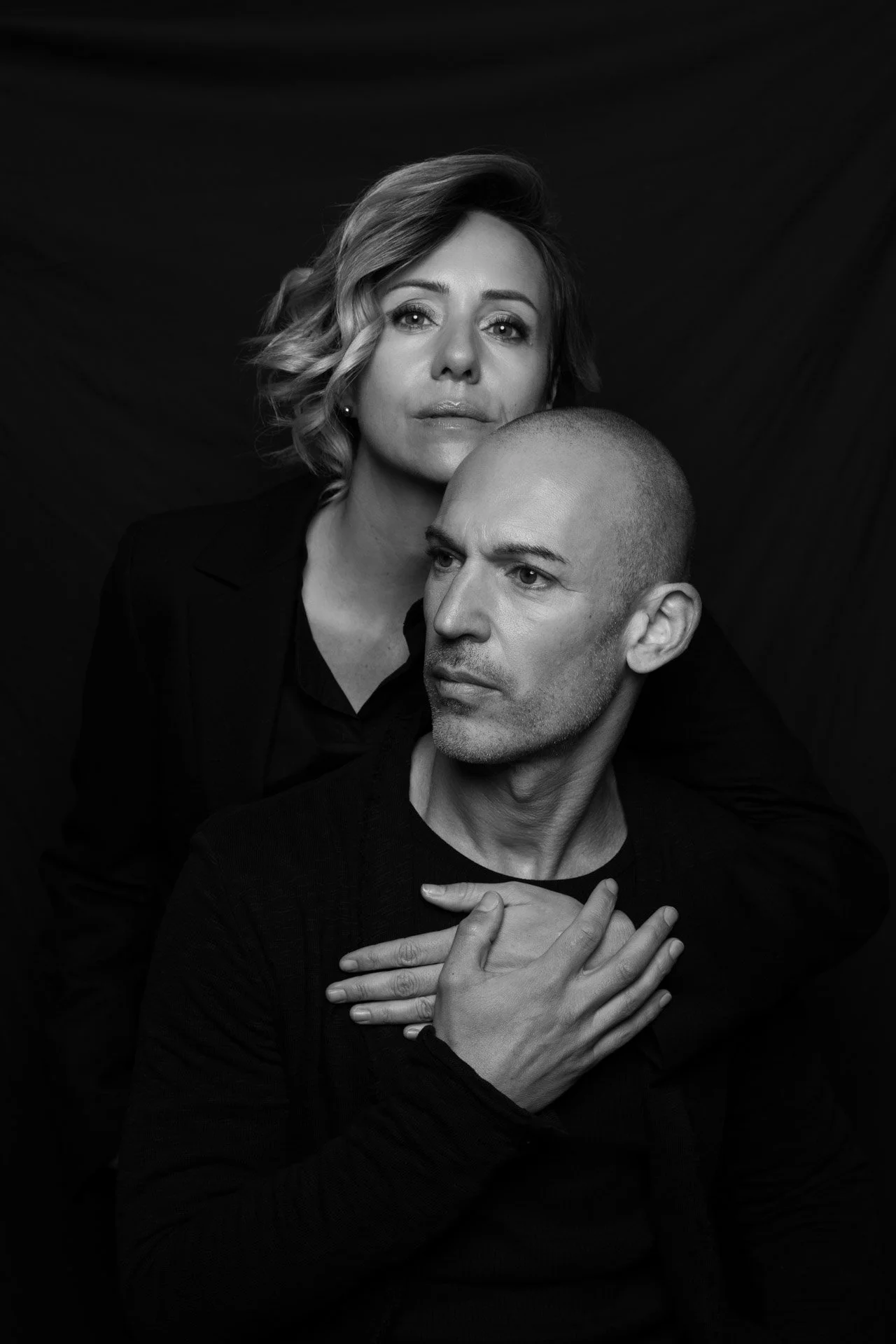 Black and white portrait of a man and woman in dramatic lighting, looking away from the camera.