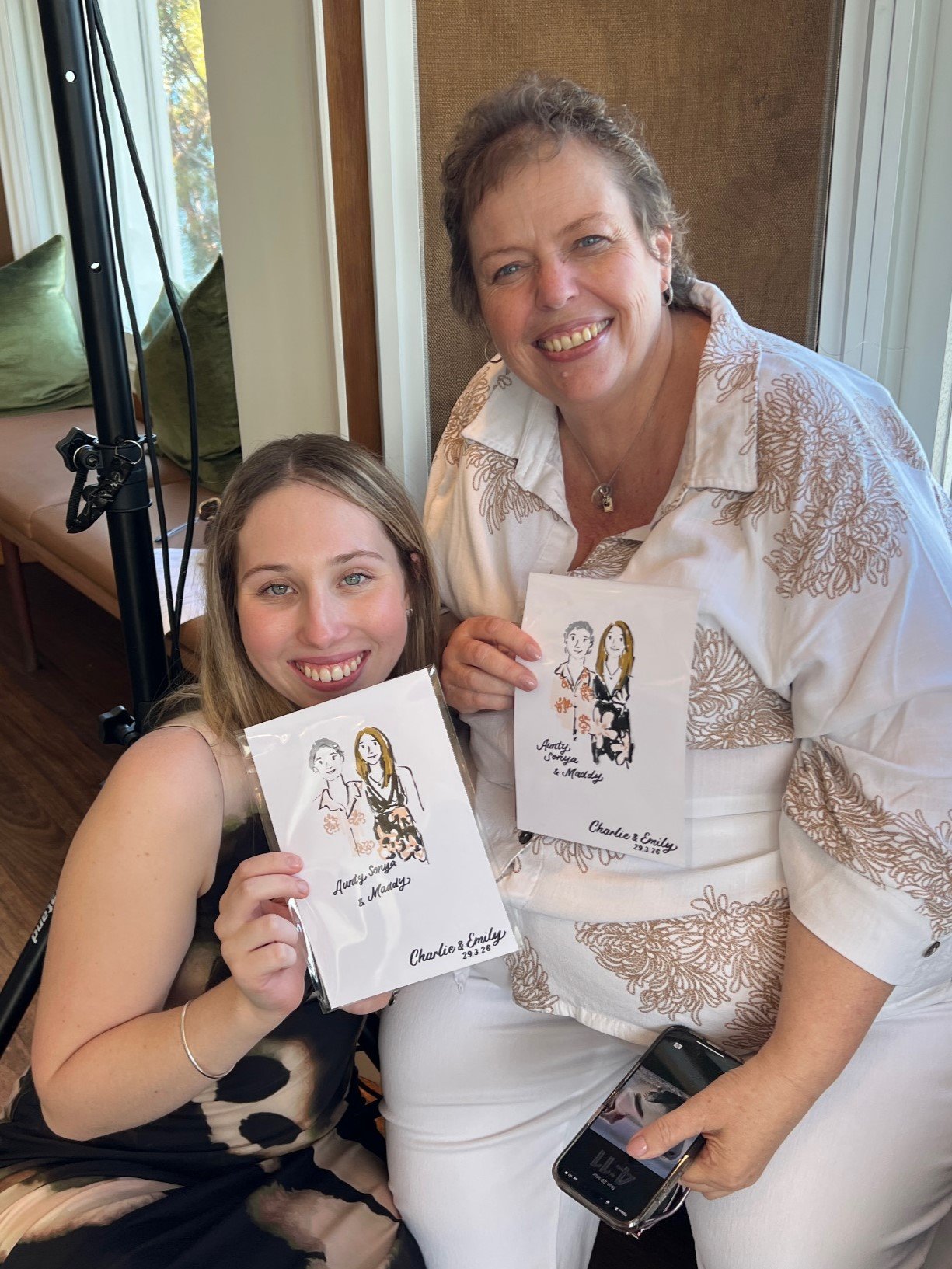Two female wedding guests smiling and posing with their personalised live illustrations at a Sydney wedding