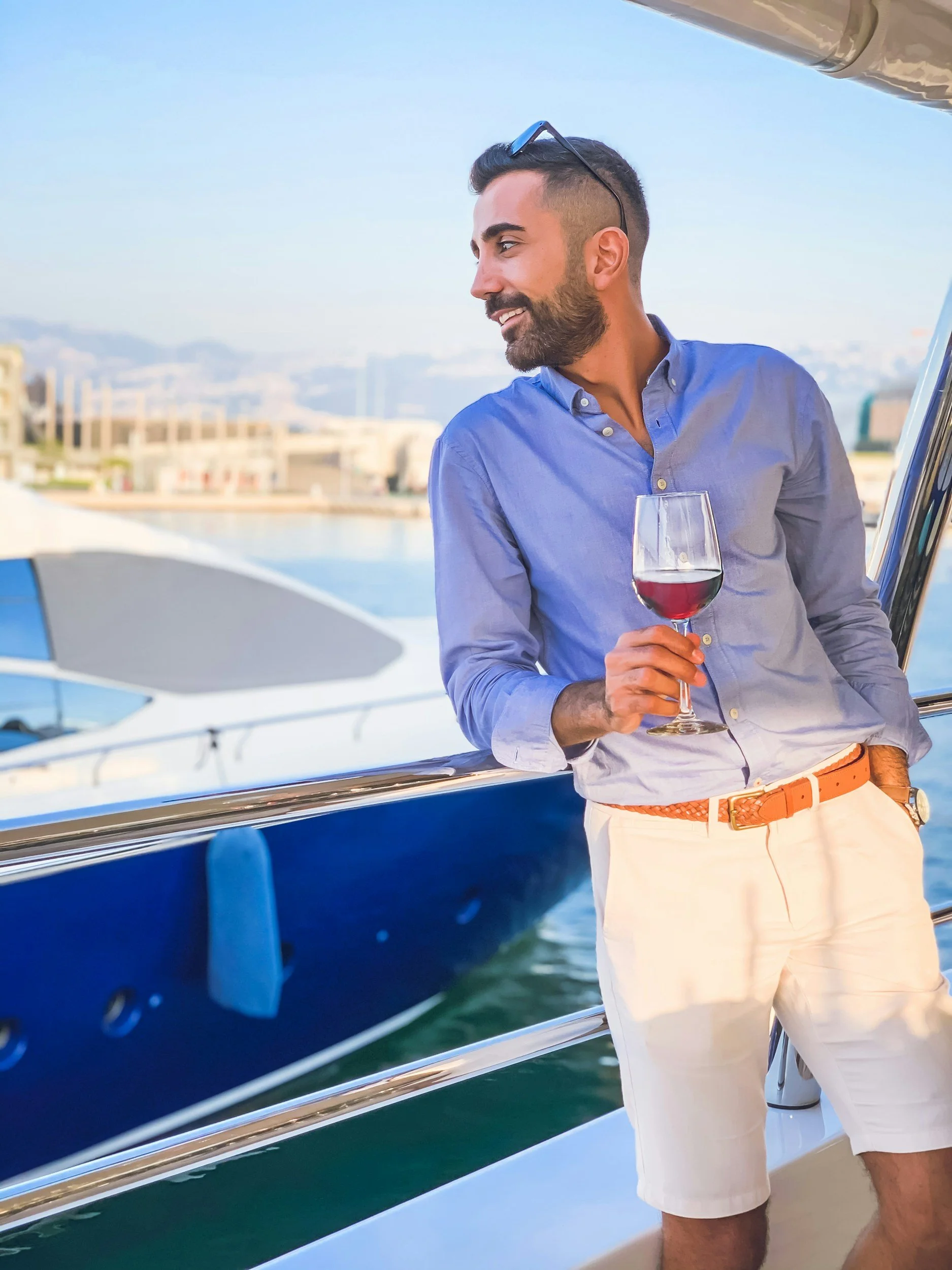 Man relaxing on a luxury yacht, holding a glass of wine and smiling while docked in a sunny marina.