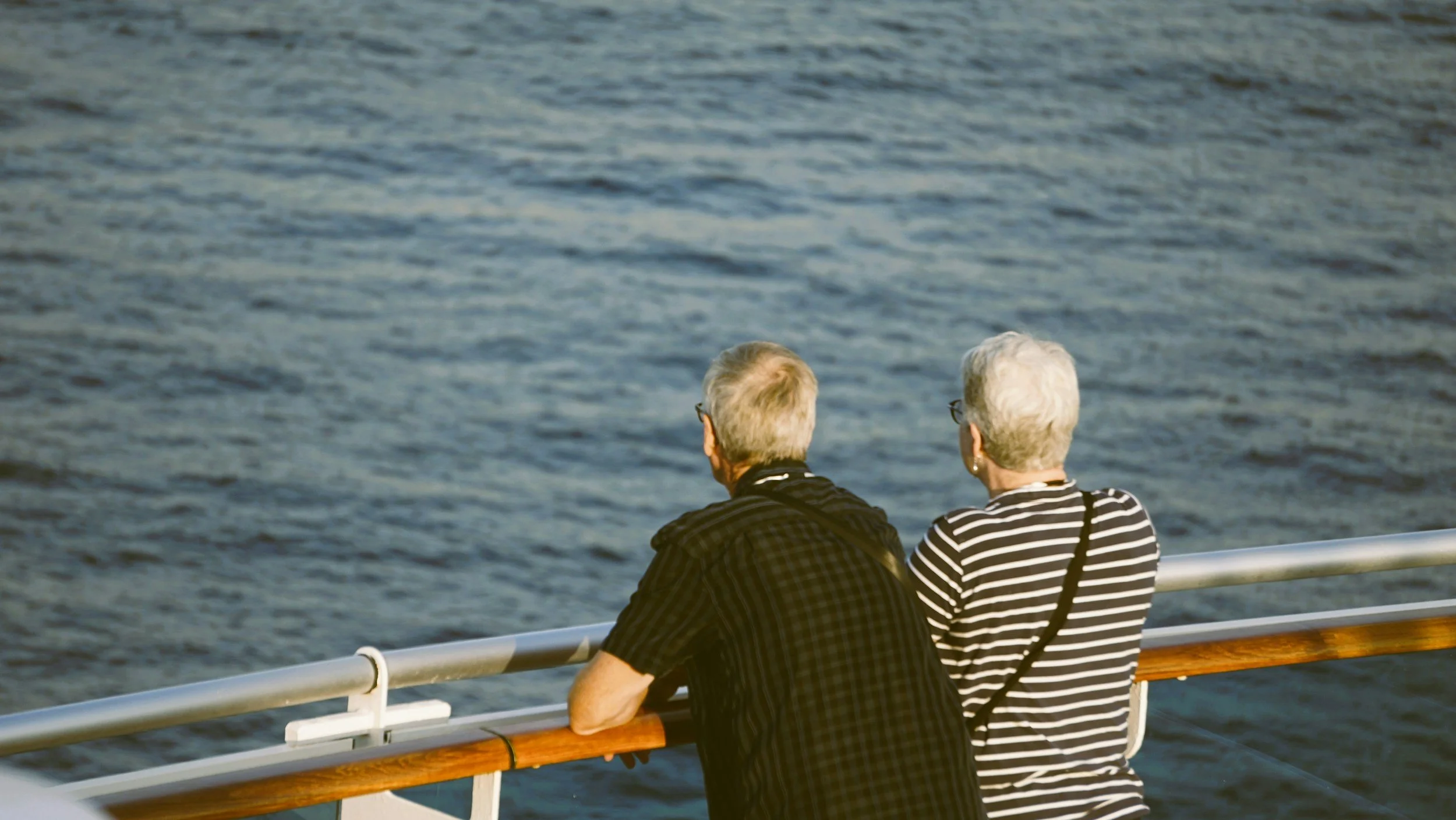 Older couple leaning on a cruise ship railing, peacefully looking out over the open sea.