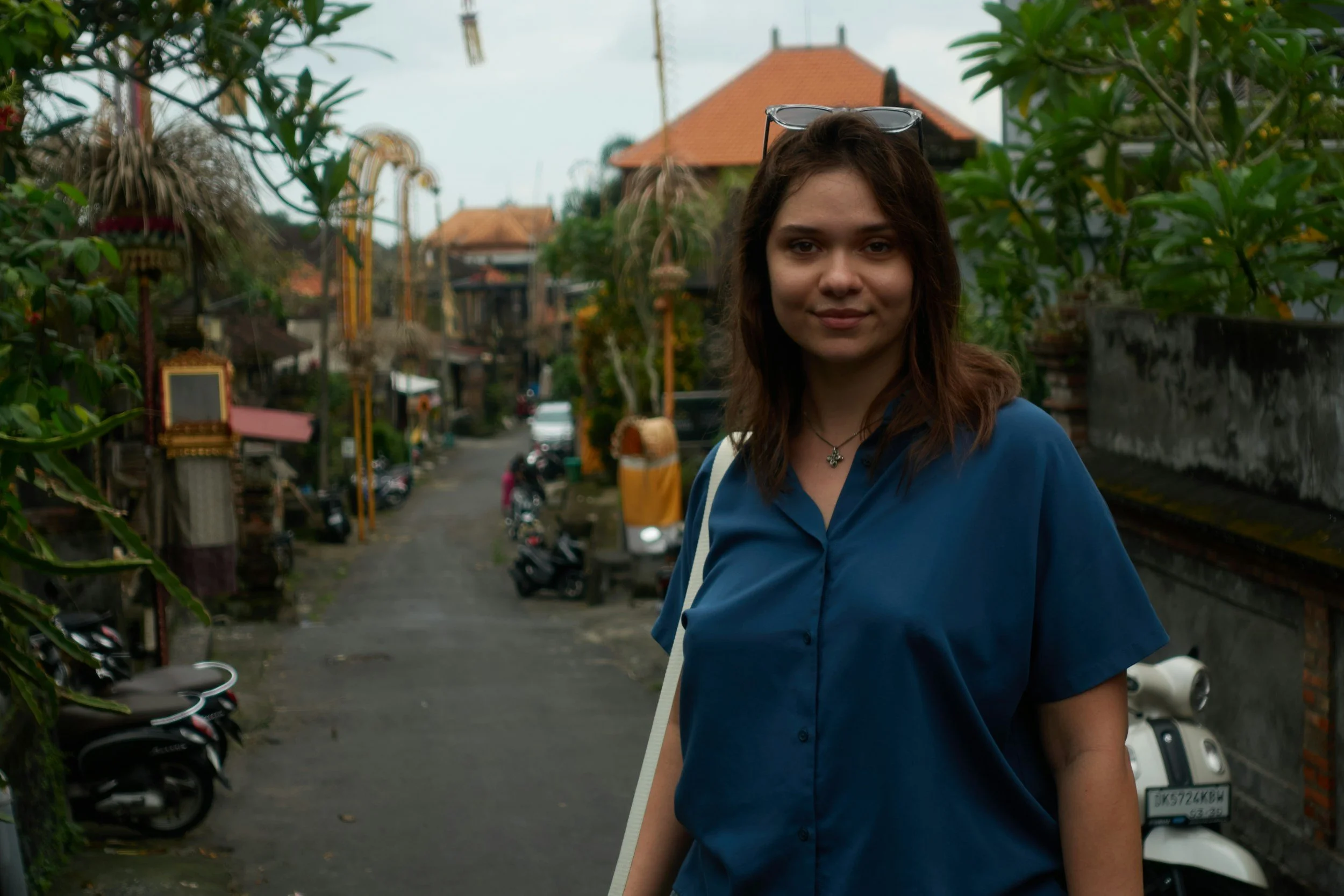 Traveler walking along a quiet street in a tropical village with scooters and traditional houses in the background.