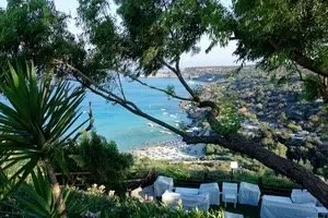 “Scenic view of a family-friendly beach in Cyprus with turquoise waters, lush greenery, and outdoor seating overlooking the Mediterranean coast.”