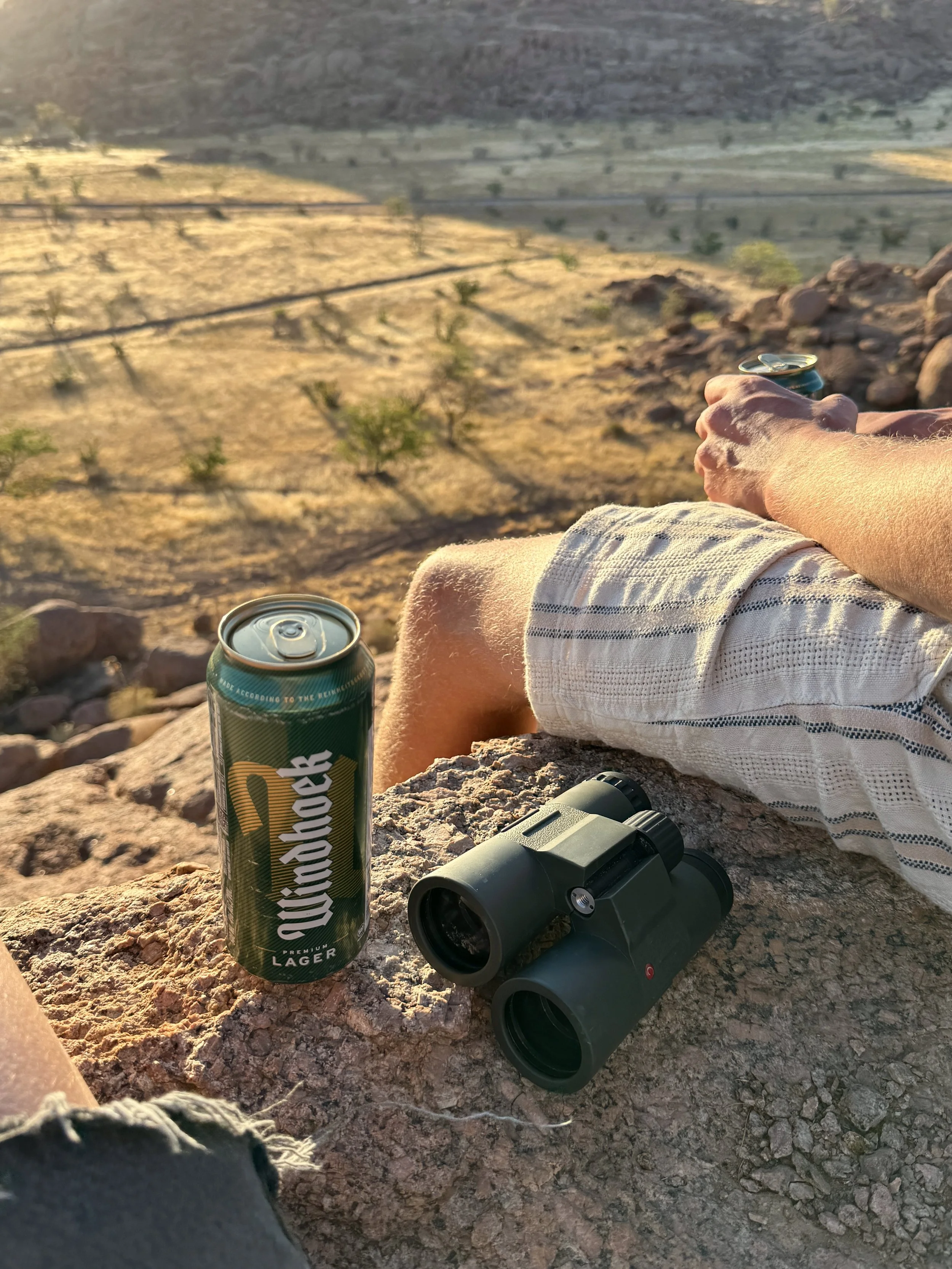 Person sitting on a rock overlooking a desert landscape in Damaraland Namibia. Golden light over the dry and vast  landscape during Namibia road trip.