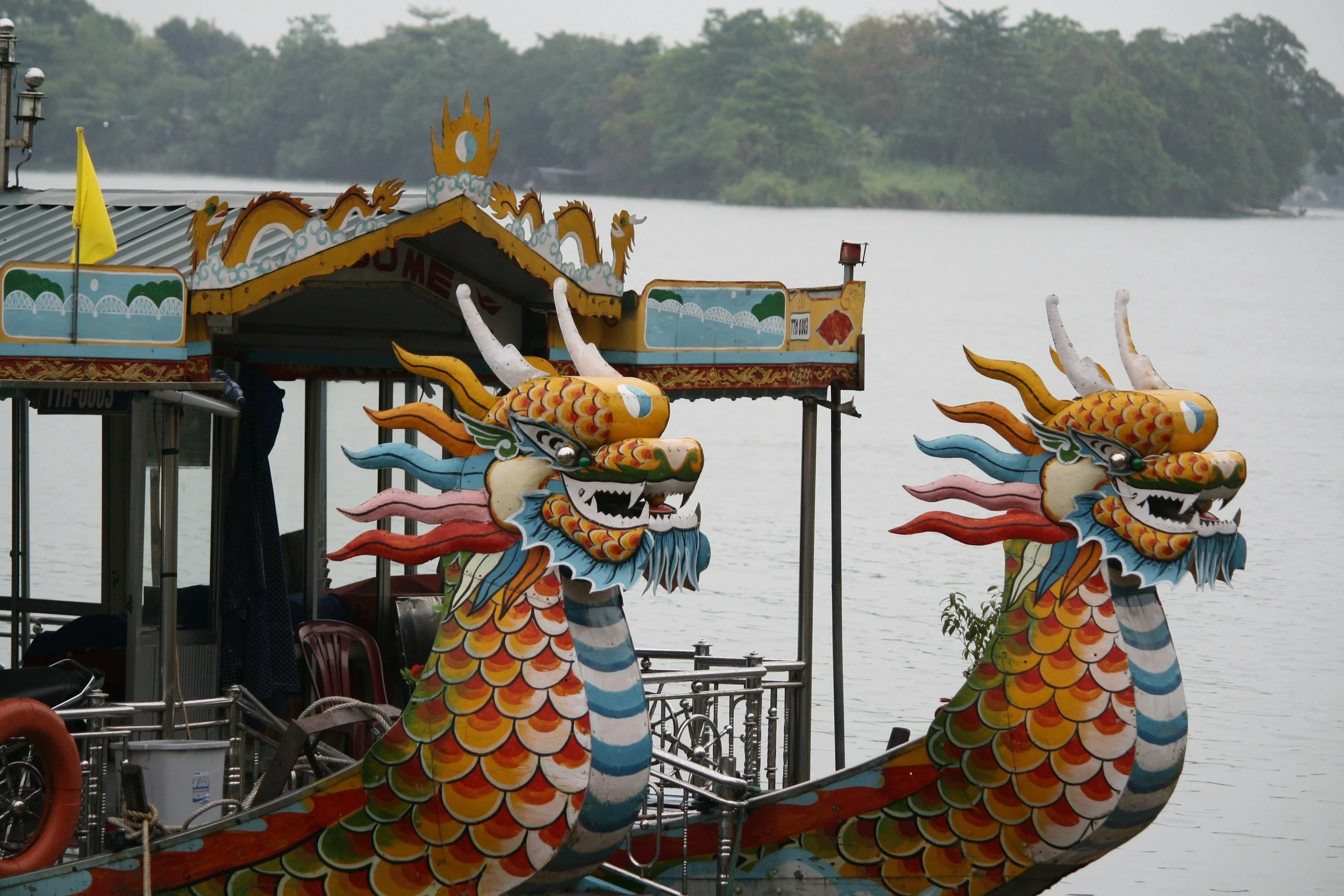 Colorful dragon boat decorations on a river with trees in the background.