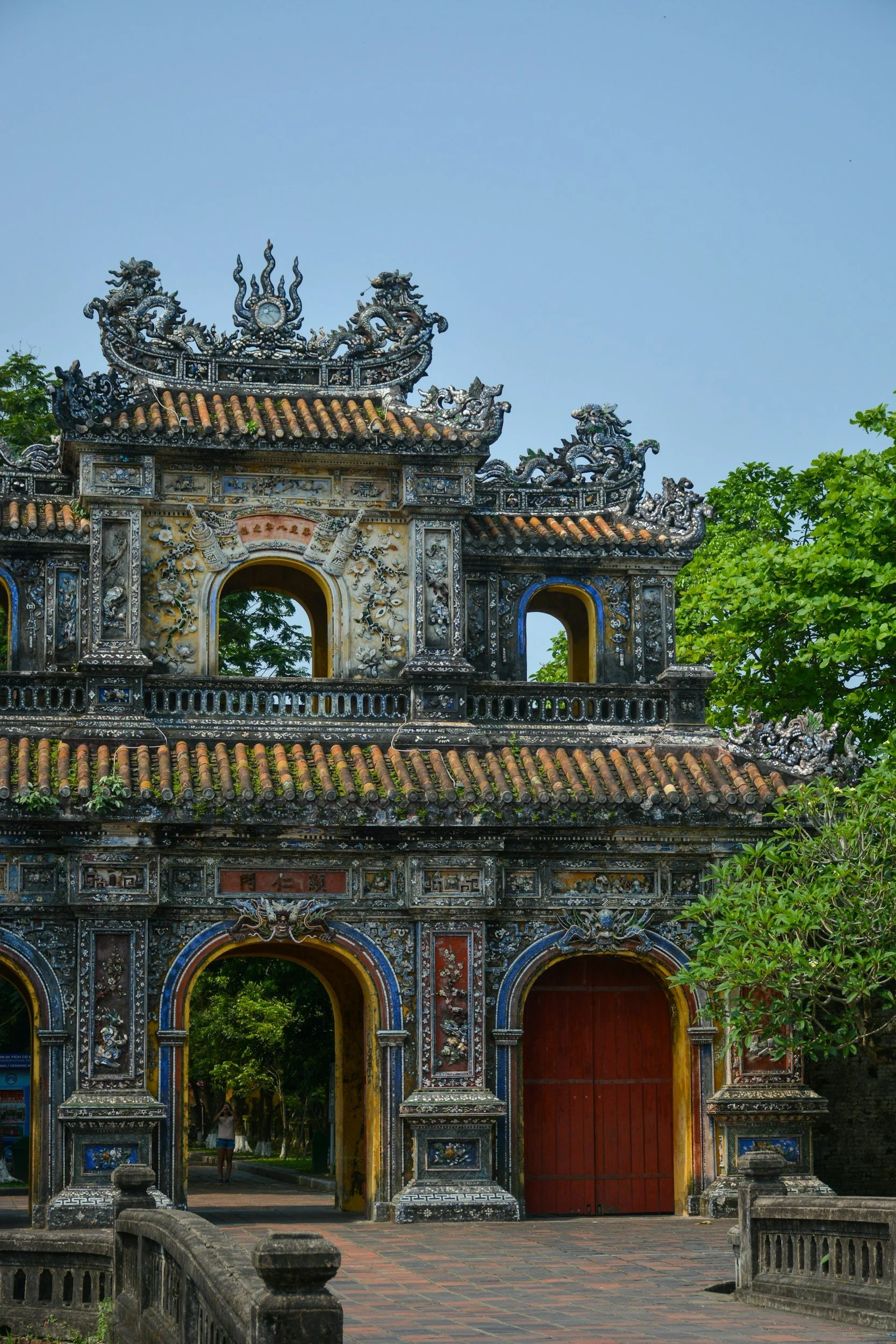 Ancient ornate gate with intricate carvings and tile roof, surrounded by greenery.