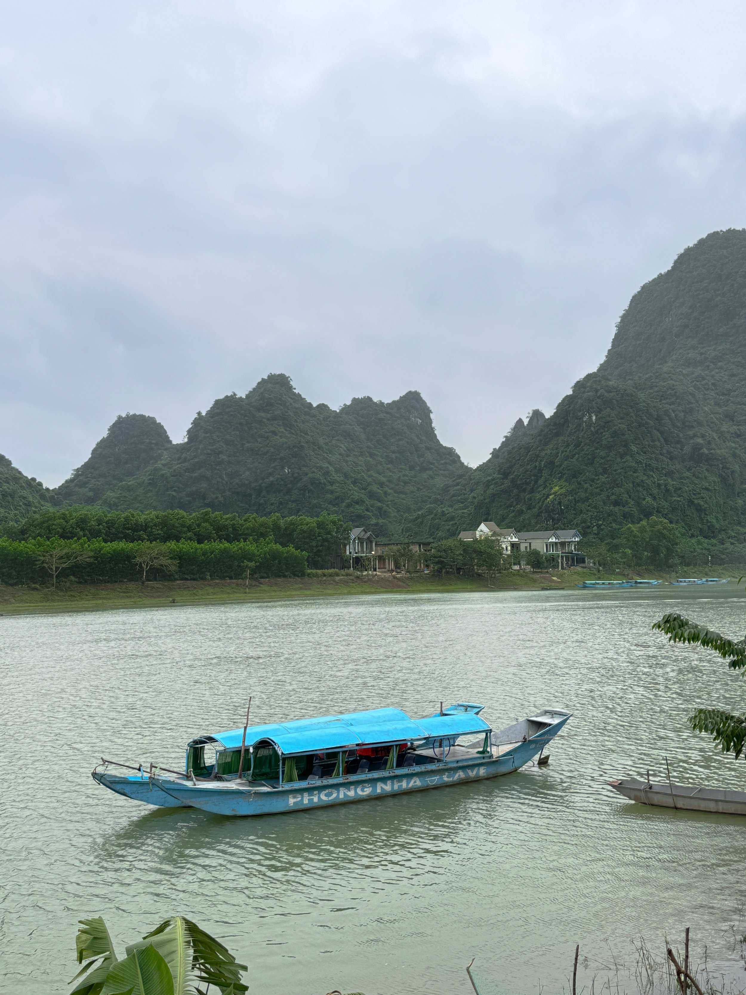 Traditional boat with blue canopy on river, surrounded by lush green mountains and trees.