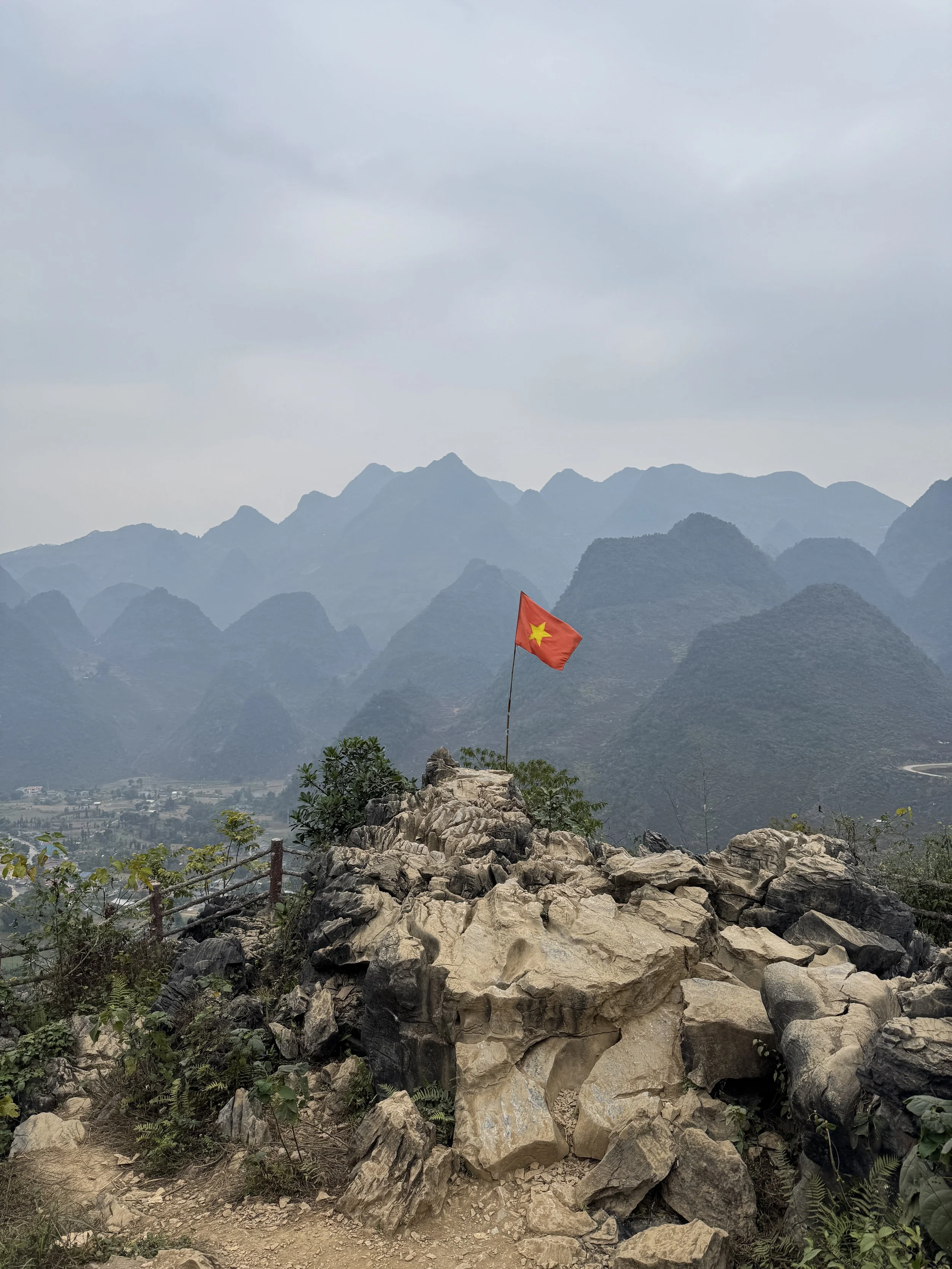Vietnamese flag atop rocky hill with mountainous landscape
