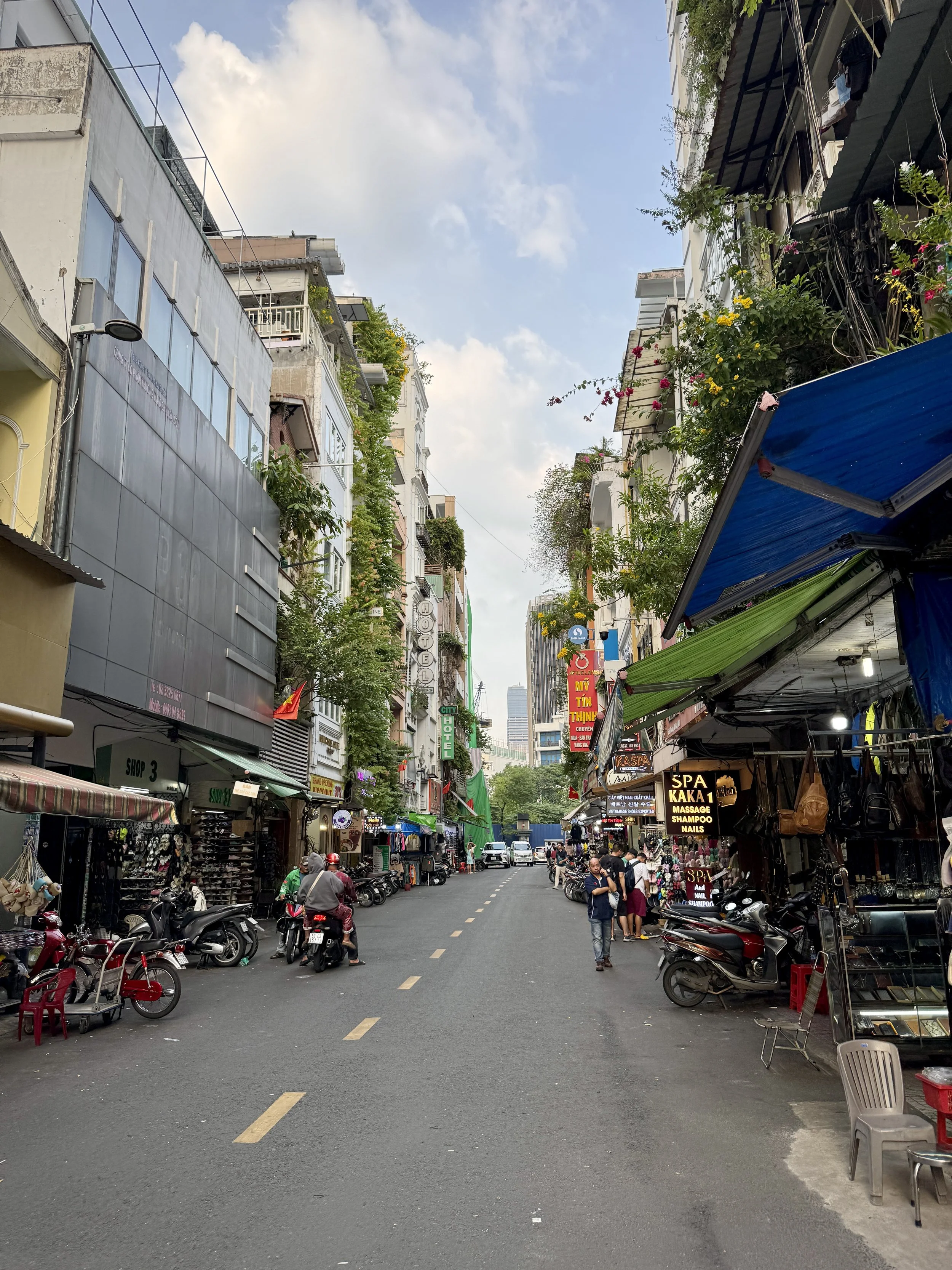Urban street scene with buildings, shops, motorcycles, and pedestrians in a city.
