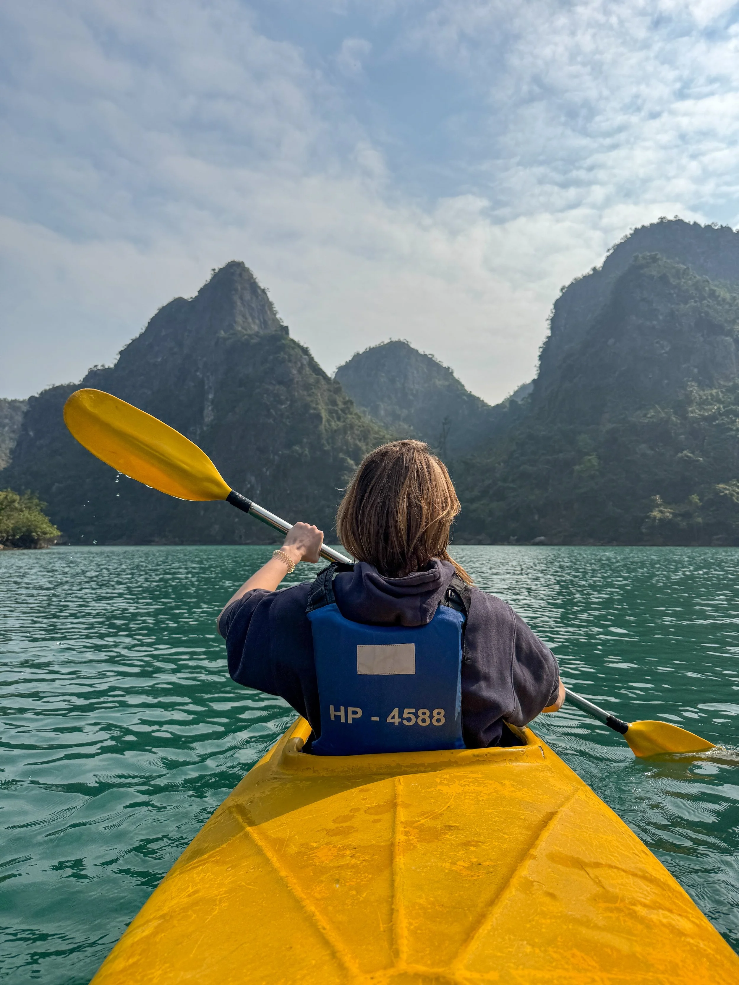 Person kayaking on a calm river surrounded by mountains, under a partly cloudy sky.