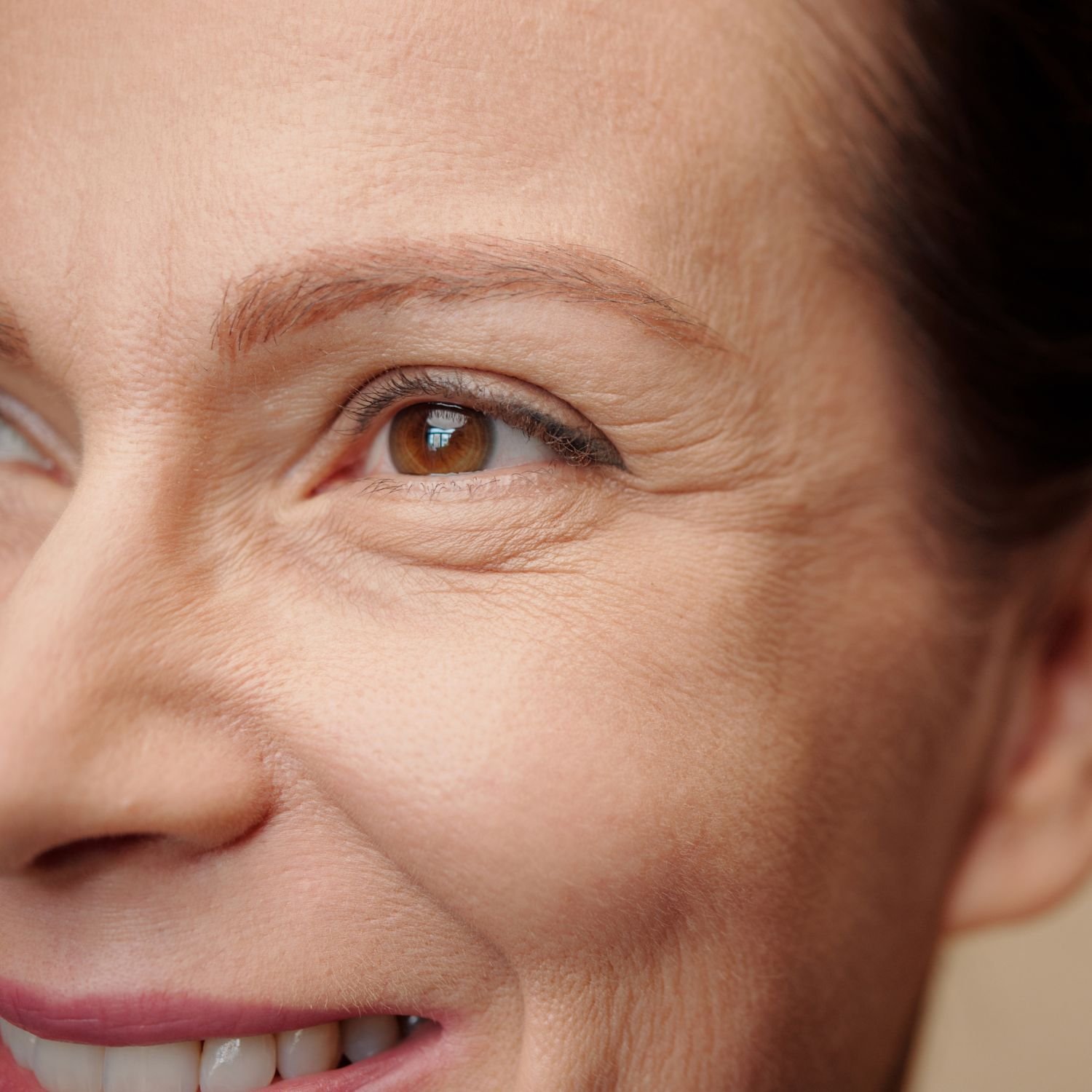 Close-up of a smiling woman's face, showing her eye, cheek, and part of her mouth with white teeth.