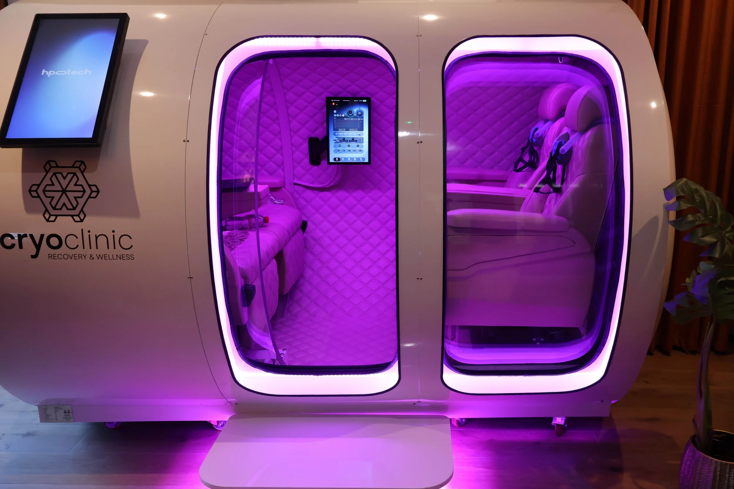 A CryoClinic chamber with purple lighting, containing seating with seatbelts inside.