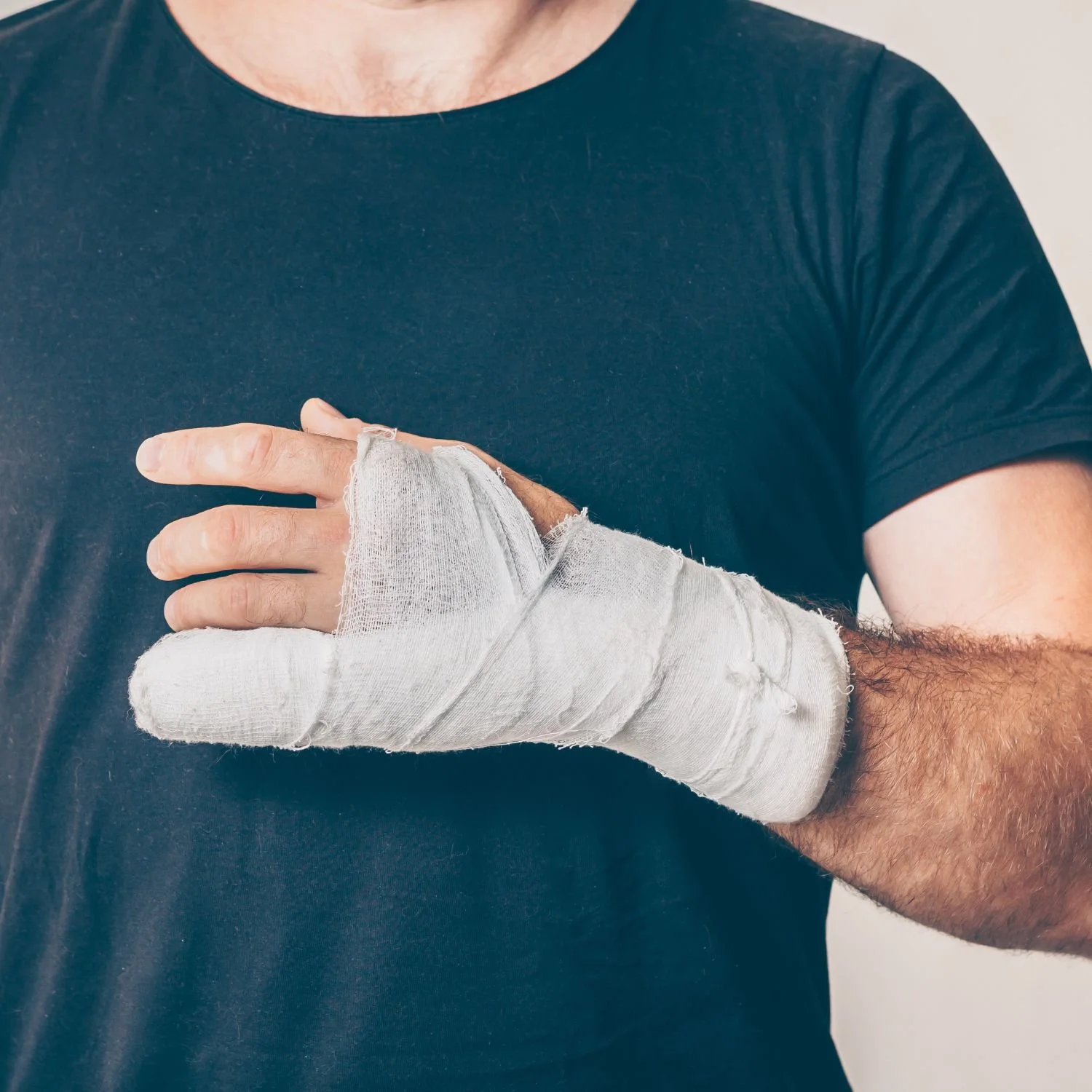 A person wearing a black T-shirt with a white bandaged hand, making a peace sign.