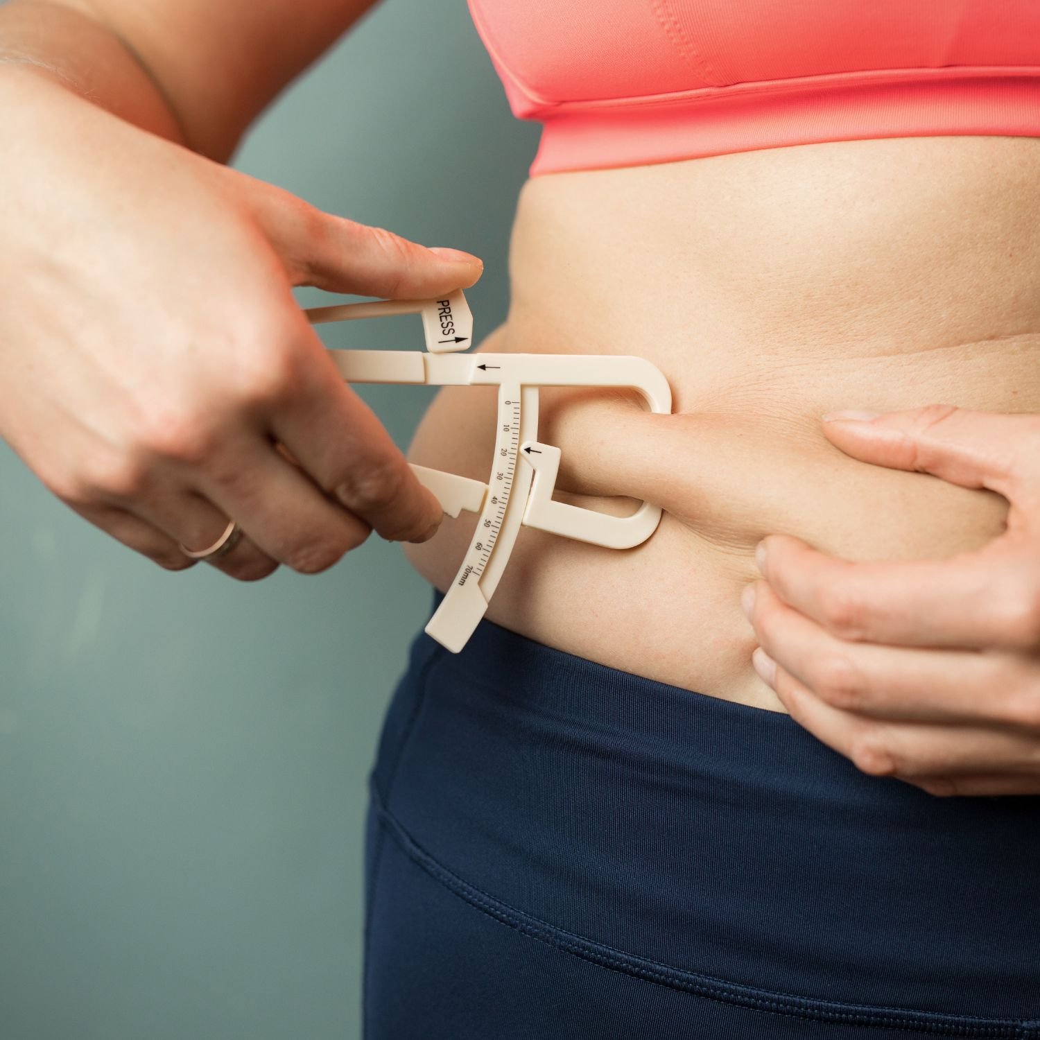A person using a skinfold caliper to measure body fat on their waist.