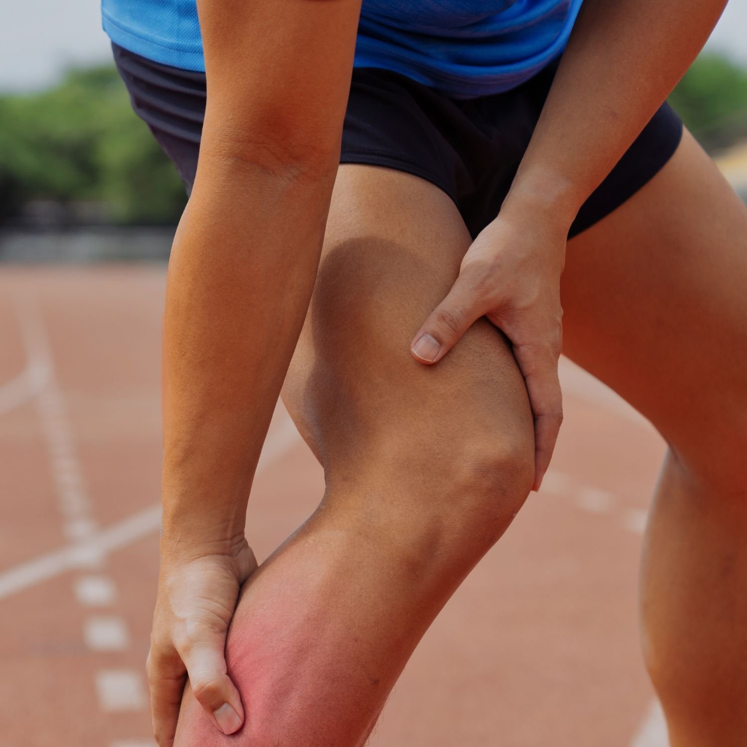 Close-up of an athlete clutching her knee, appearing to experience pain, on a running track.