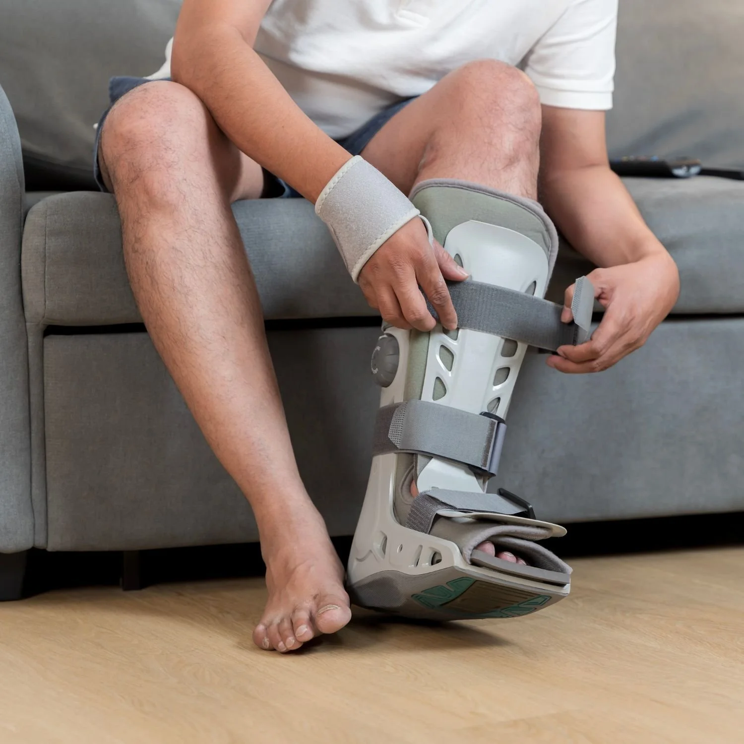 A woman with dark hair in a bun looks at herself in a mirror, holding her cheeks with both hands, with a surprised or shocked expression.