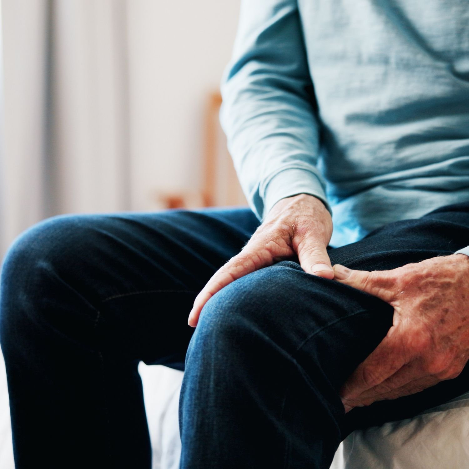 Older person experiencing knee pain, holding their knee with one hand