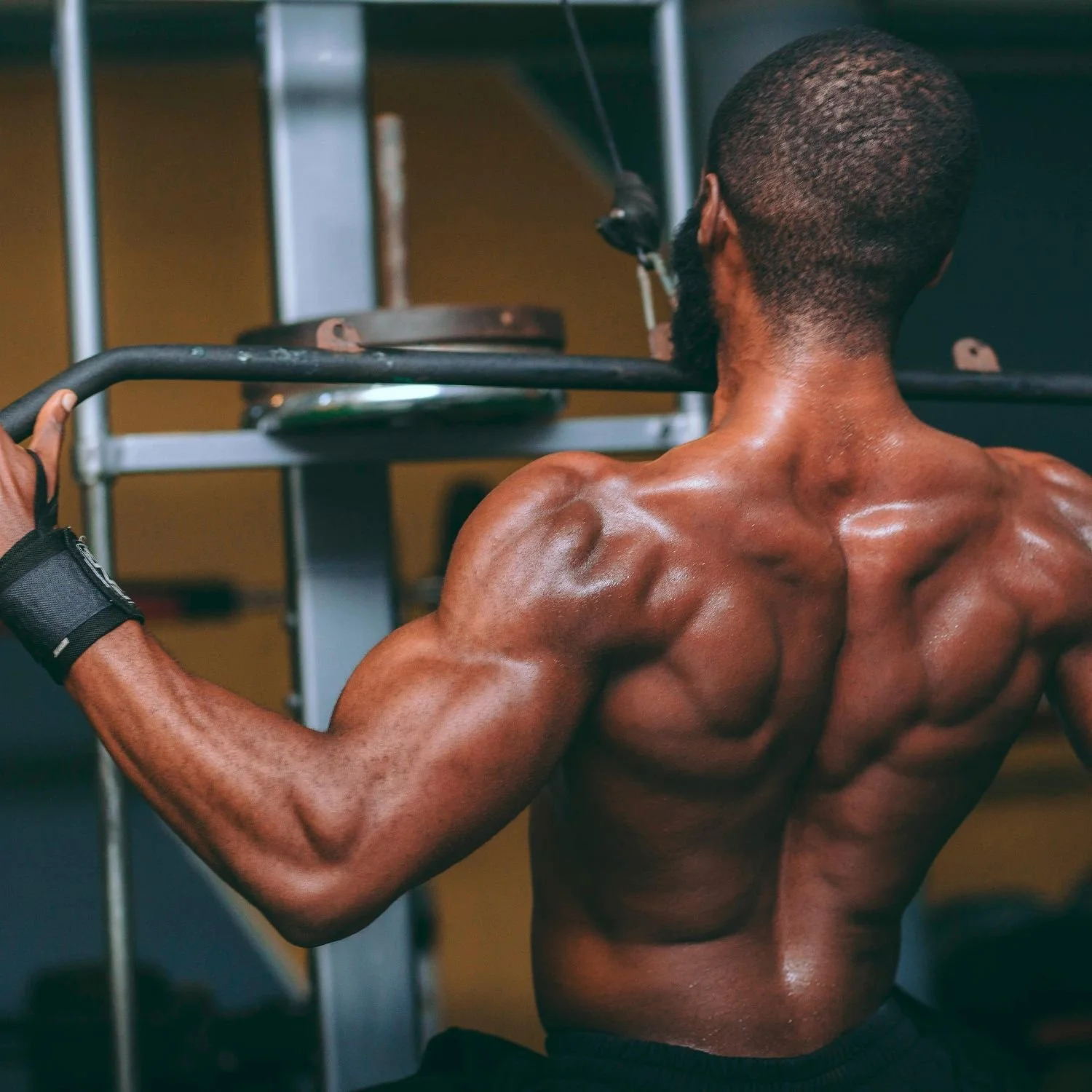 A muscular man with dark skin and short hair doing a shoulder exercise at the gym.