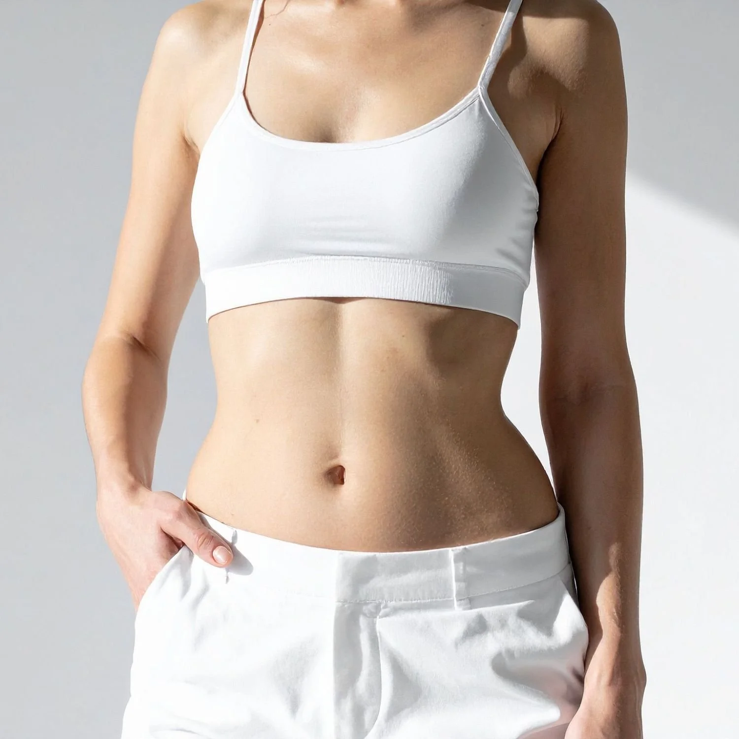 Close-up of a woman in a white sports bra and white pants, showcasing her toned stomach and midsection.