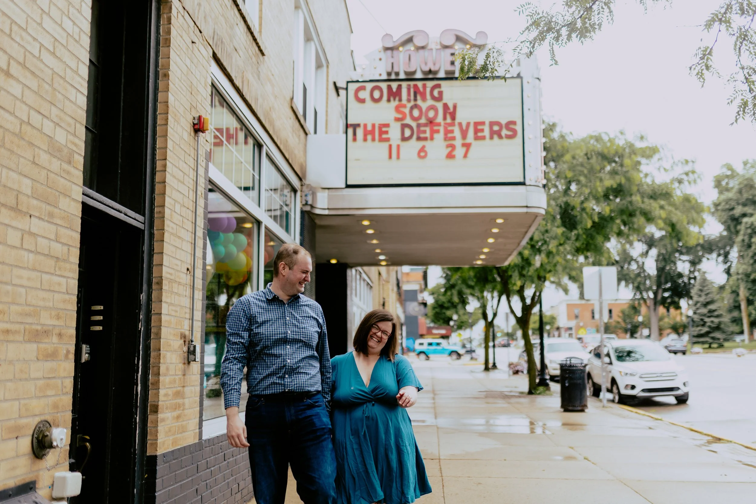 Detroit engagement photographer capturing a couple walking beneath the Historic Howell Theater marquee during their downtown Howell engagement session.