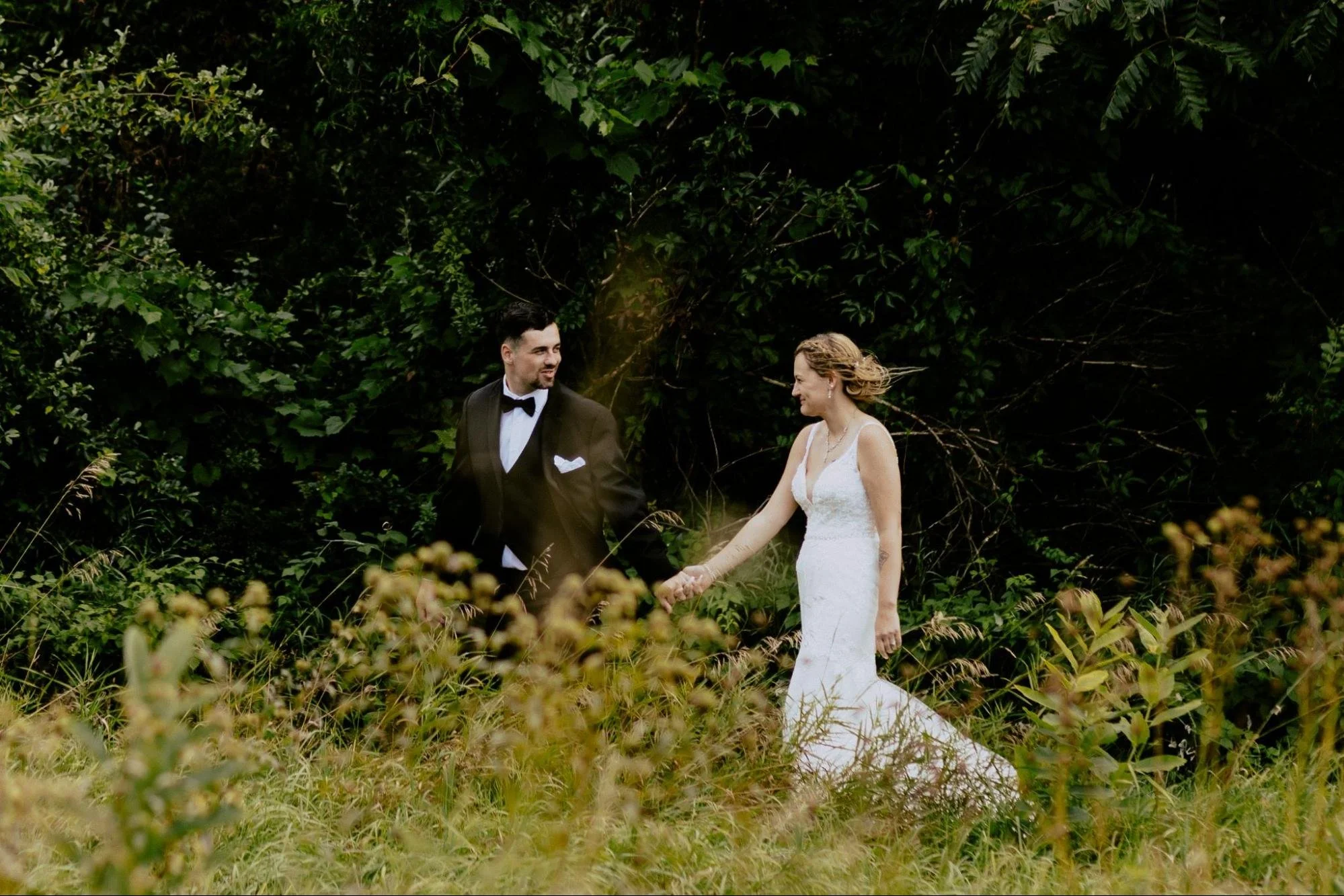 Detroit wedding photographer capturing a bride and groom holding hands during romantic outdoor wedding portraits surrounded by lush greenery.