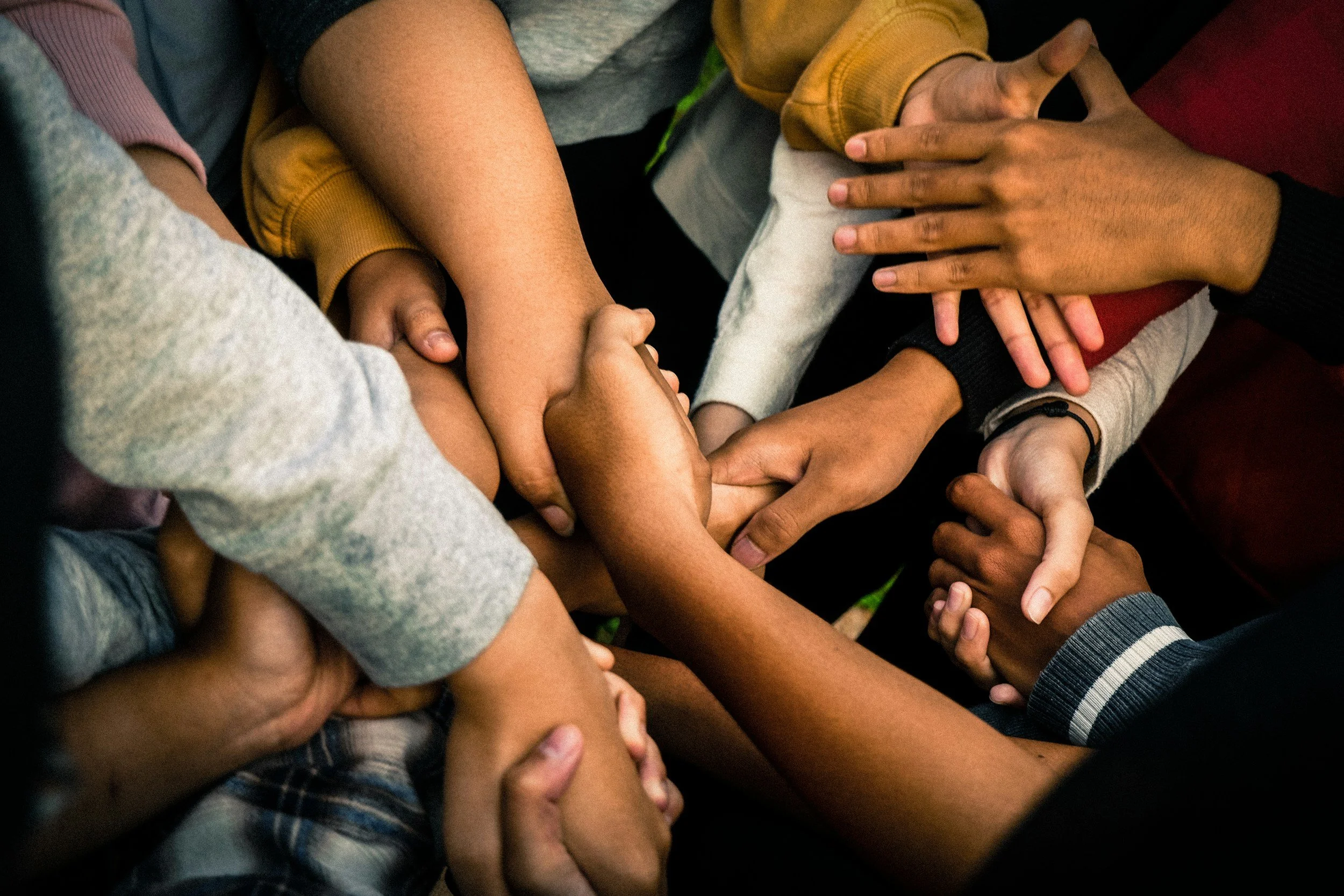 Multiple hands of diverse skin tones overlapping and holding each other in a group hug or display of unity.