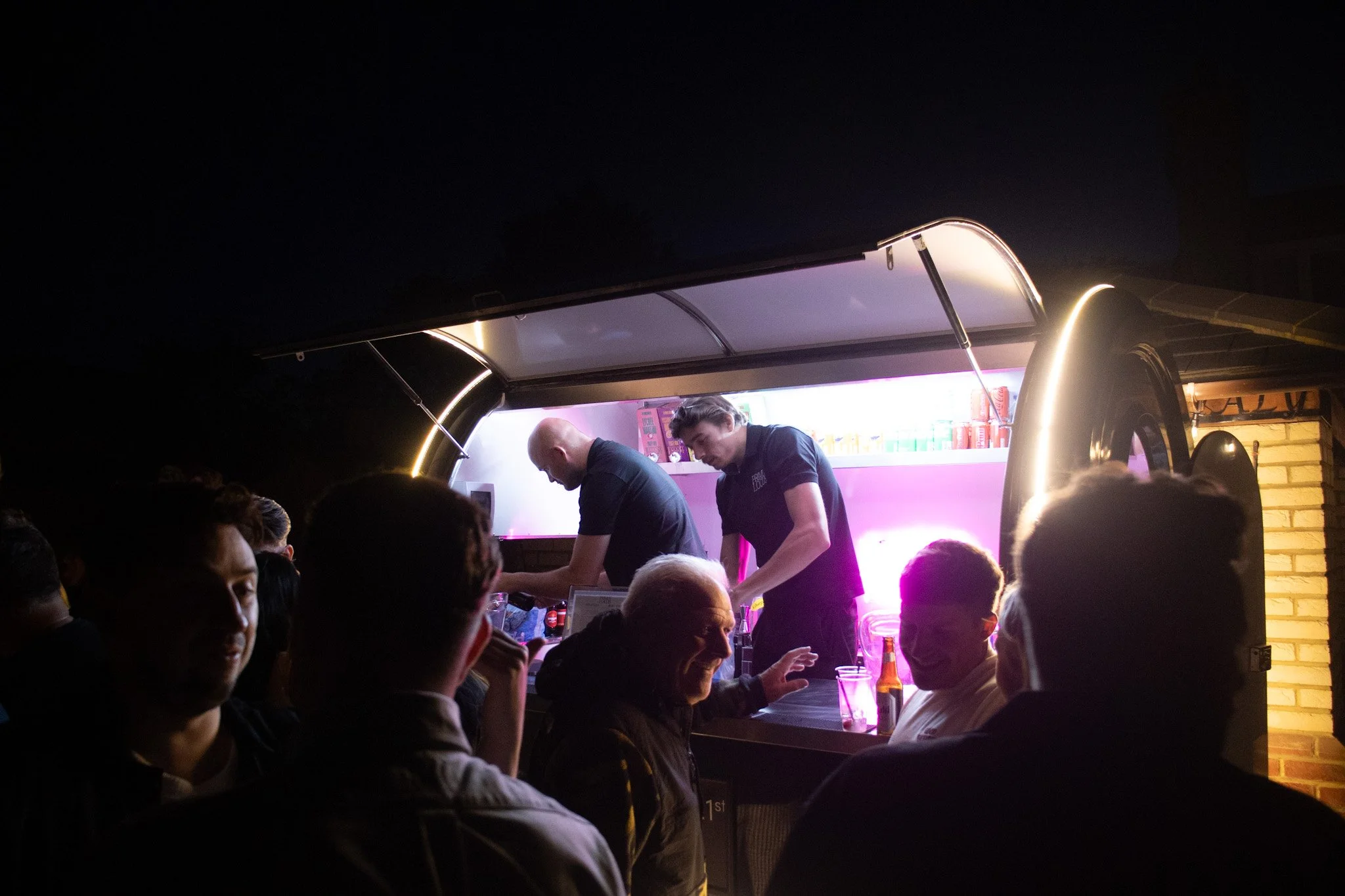 People at a food truck socializing and being served by staff at night.