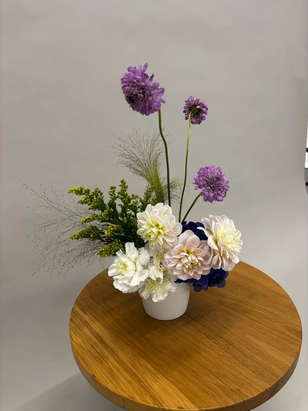 Purple, white, and cream-colored flowers in a white vase on a wooden table.